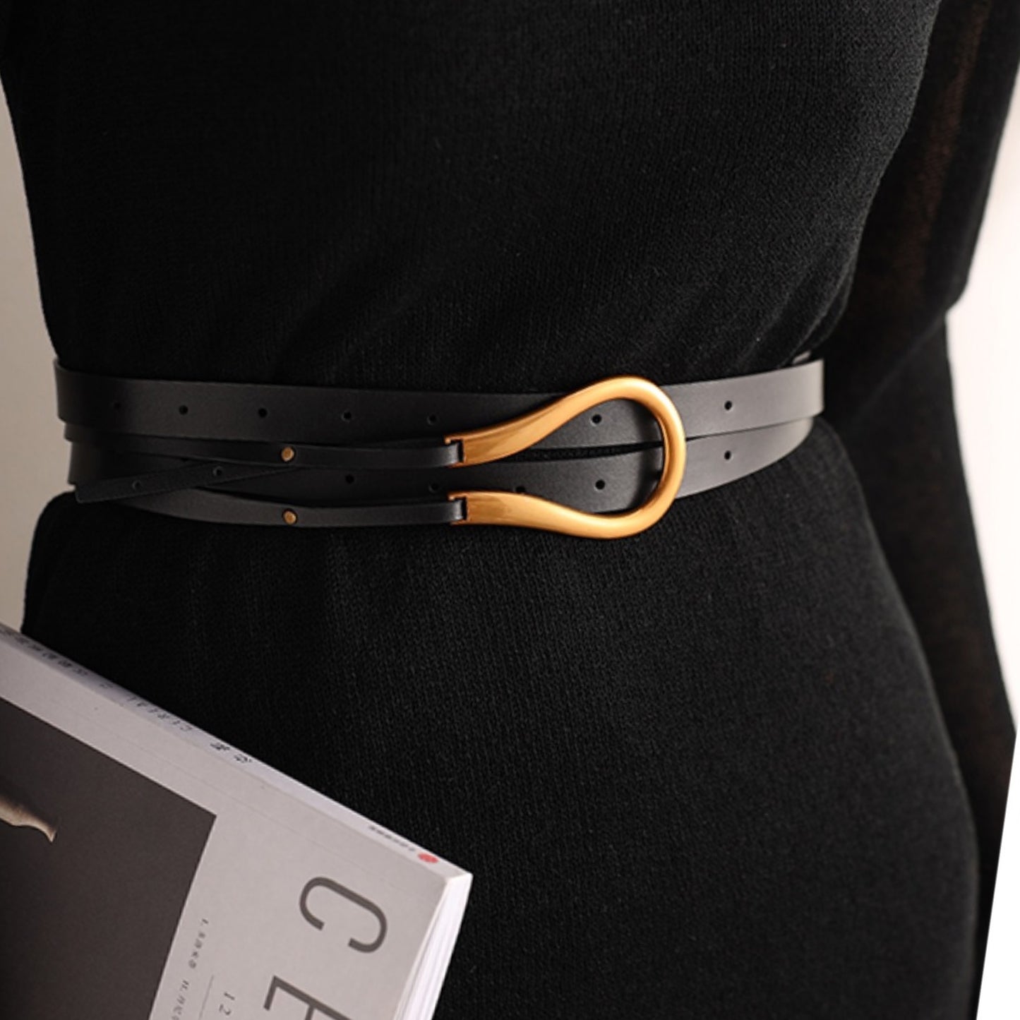 Person wearing a black belt with a gold buckle, holding a magazine.