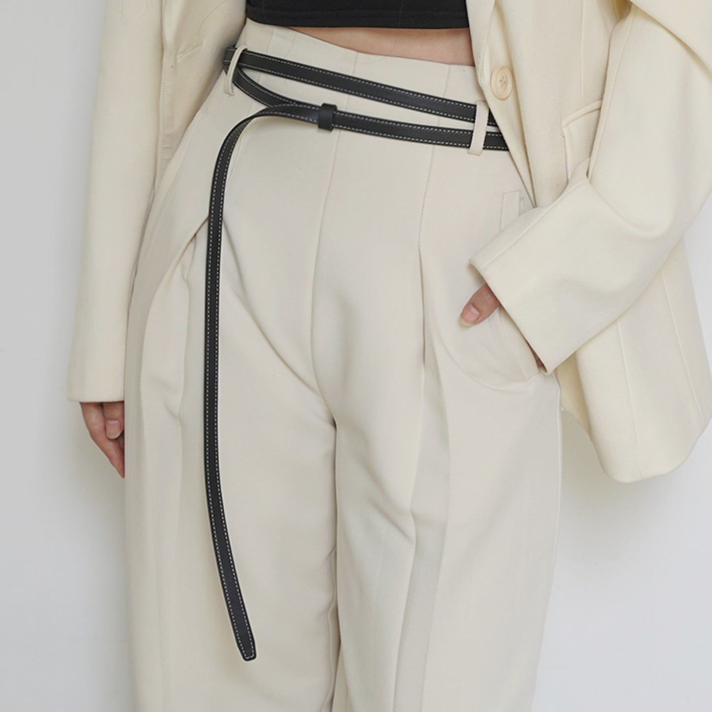 Person wearing a white coat and beige pants with a black belt against a white background