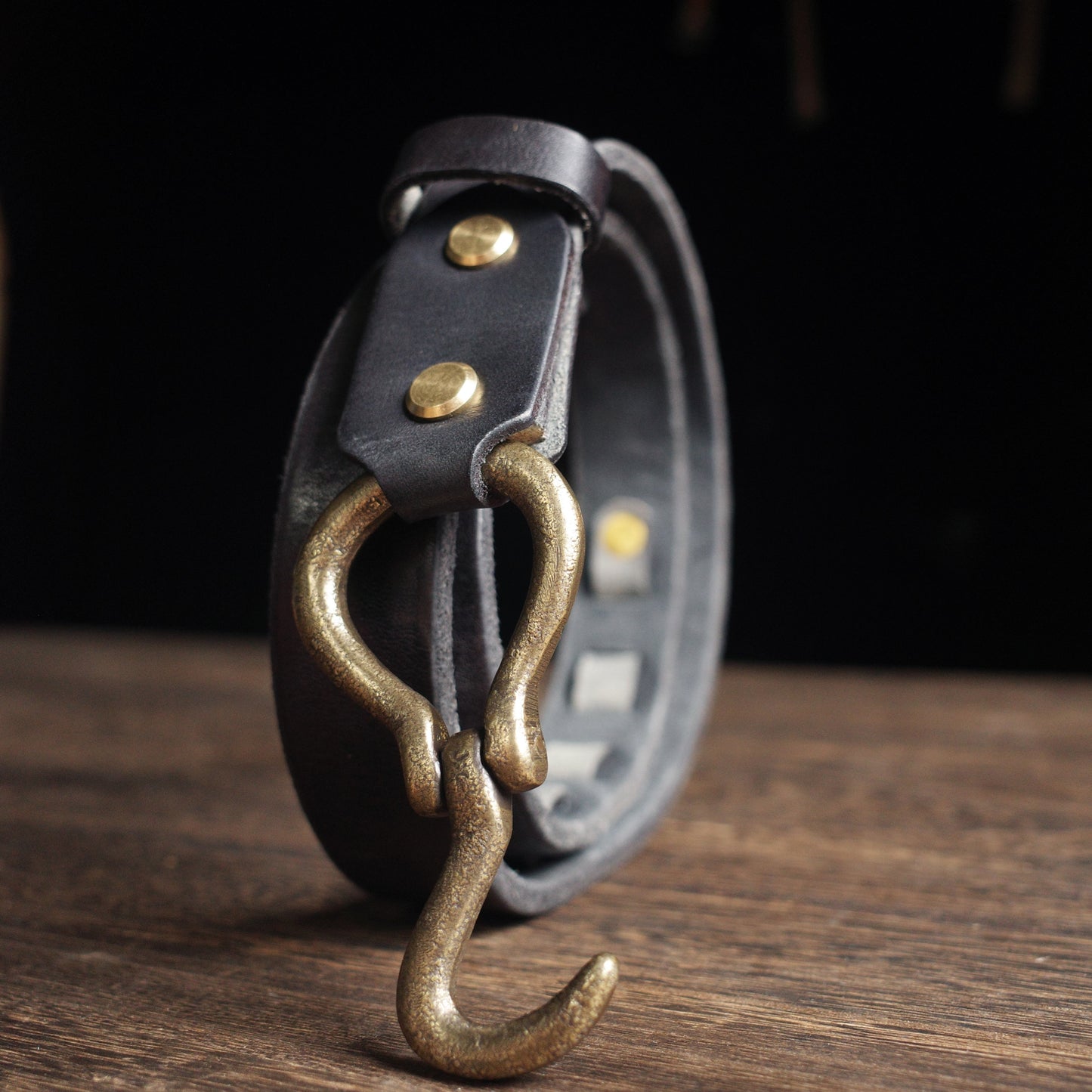 Black leather belt with brass hook on a wooden surface