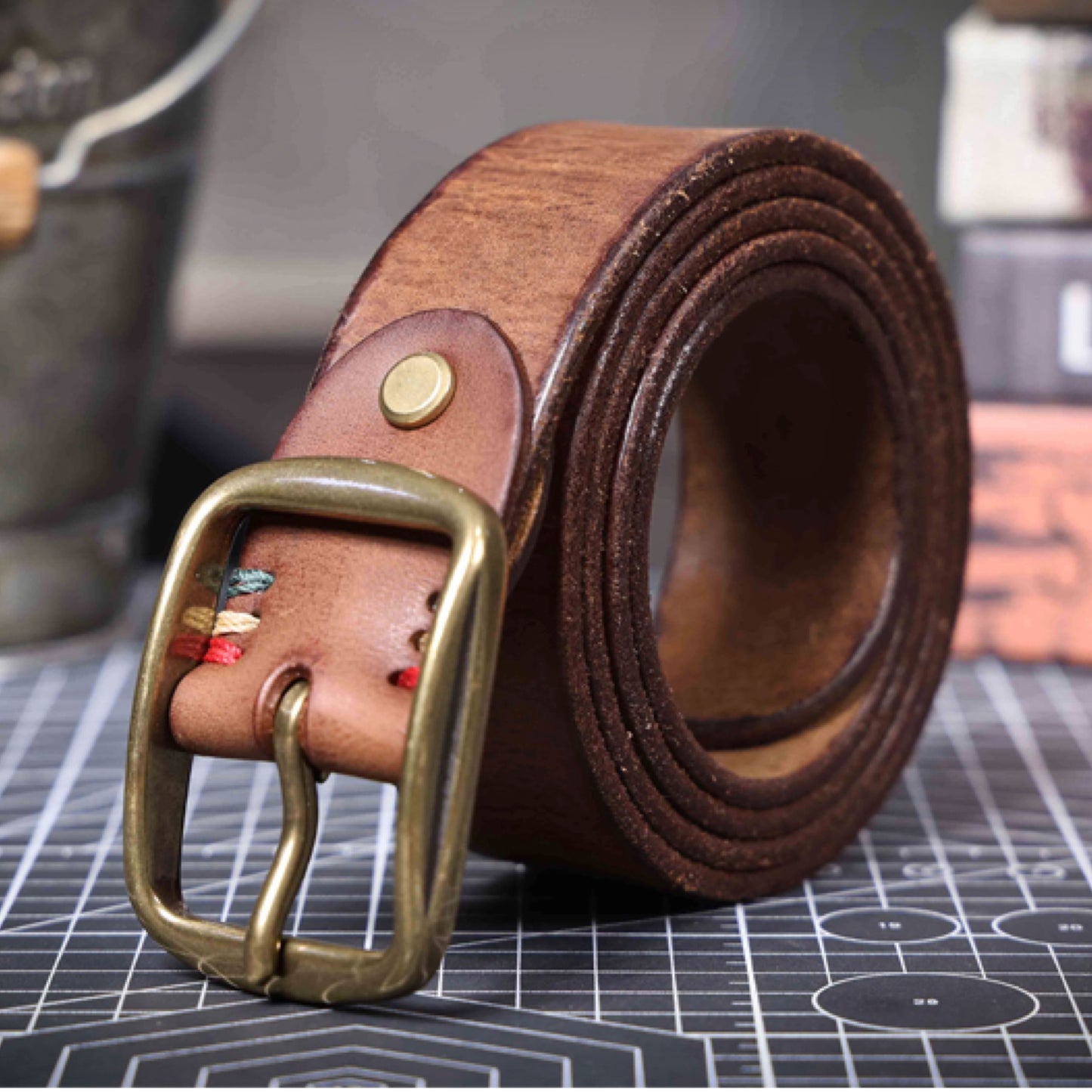 Brown leather belt with brass buckle on a grid surface