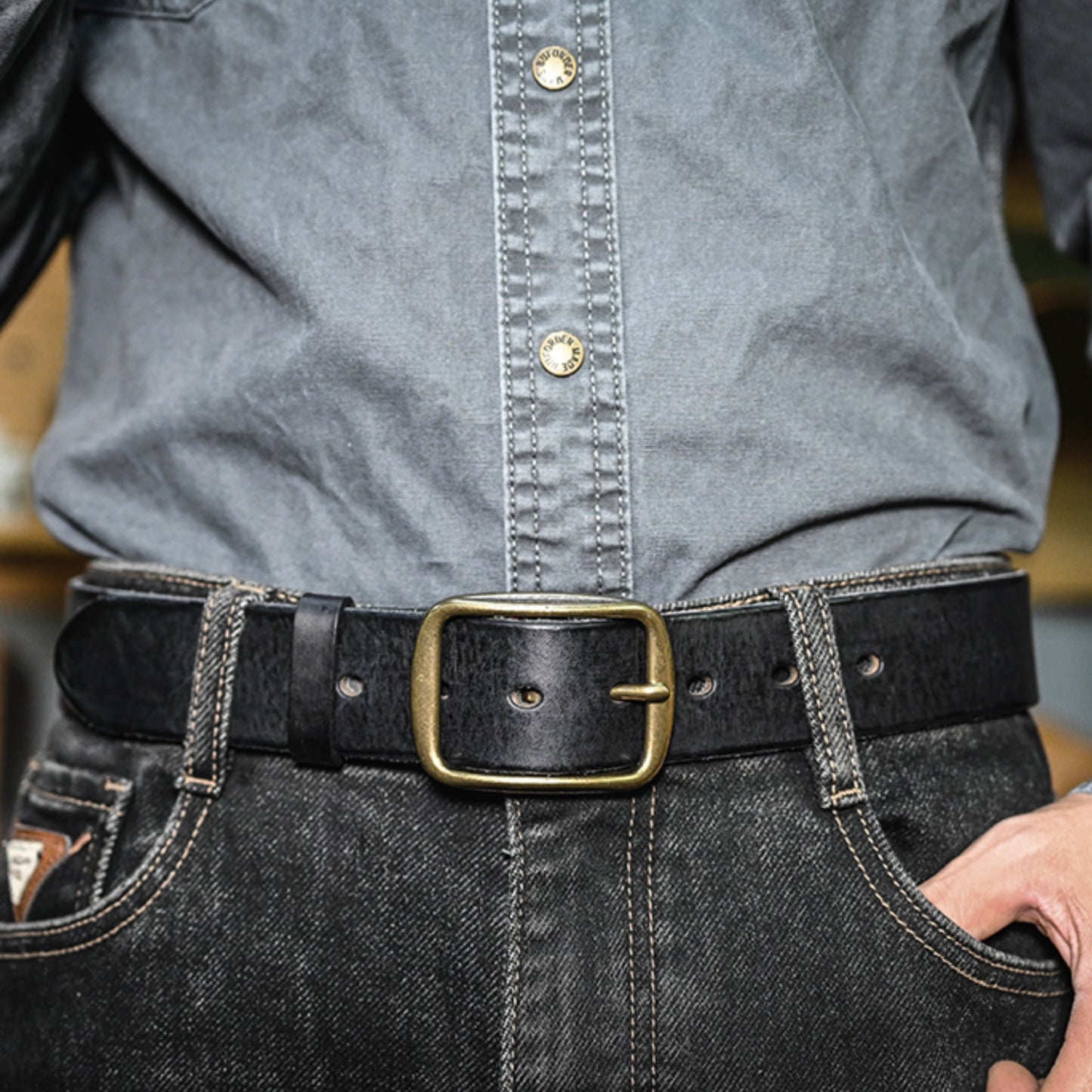 Person wearing a gray denim shirt and black jeans with a gold belt buckle.