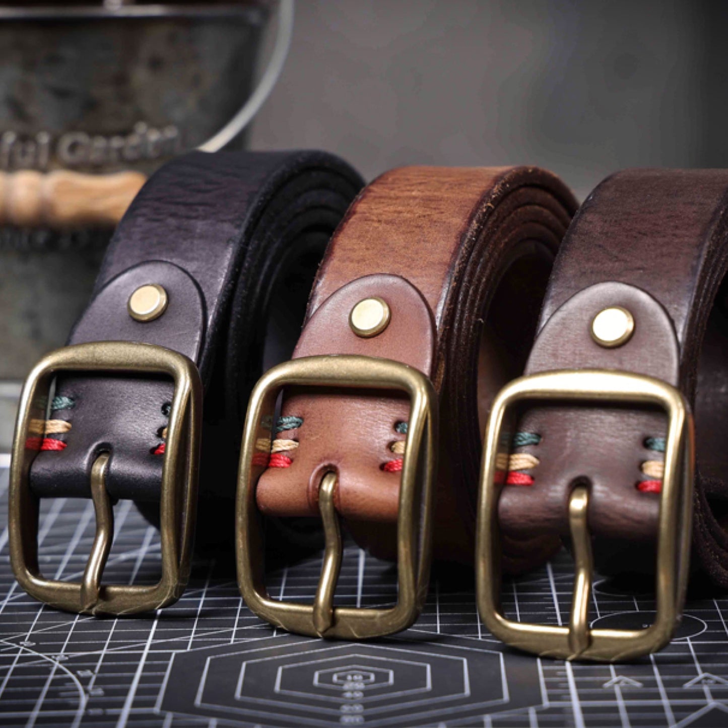 Three leather belts with brass buckles on a grid background