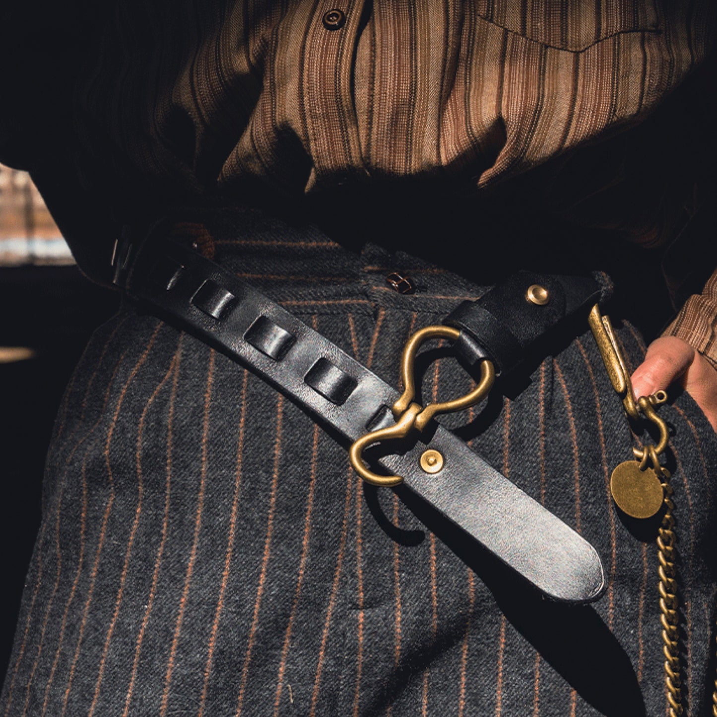 Person wearing a leather belt with gold hardware and a dog collar, standing against a blurred background.
