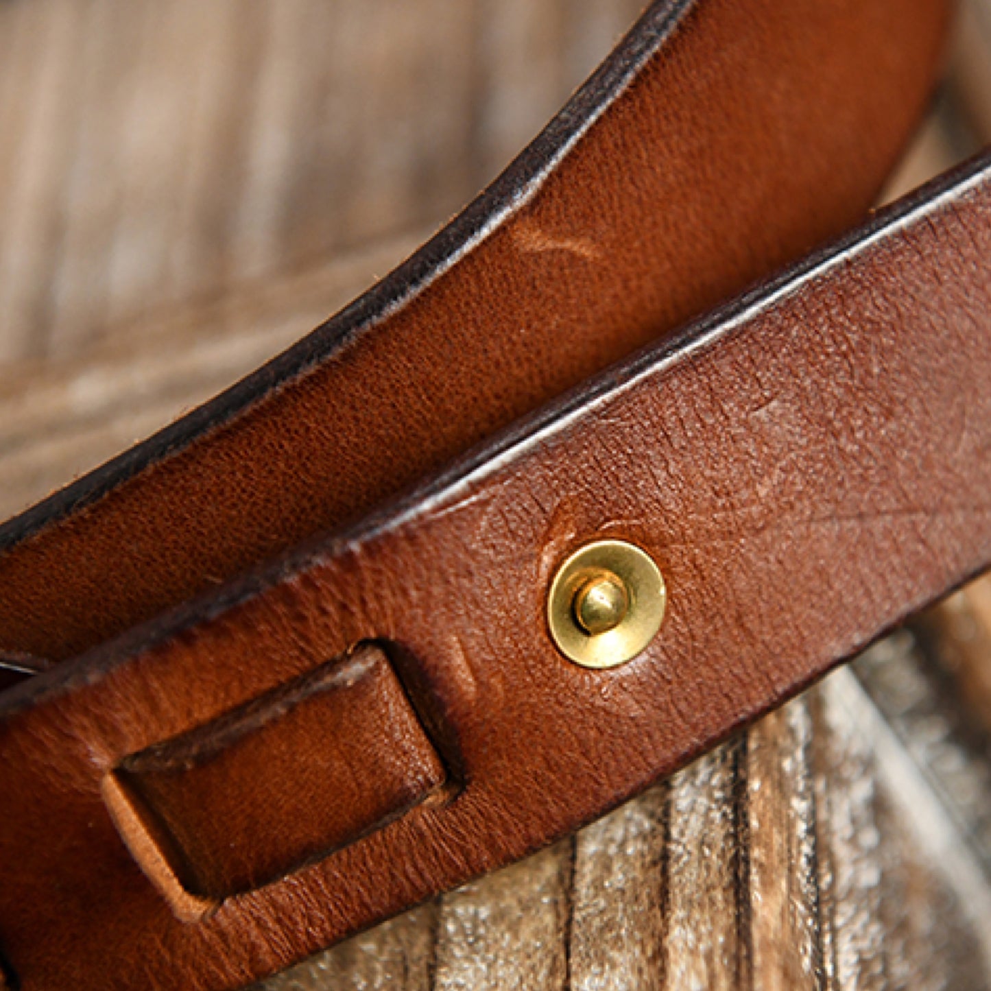Close-up of a brown leather strap with a gold buckle on a wooden surface