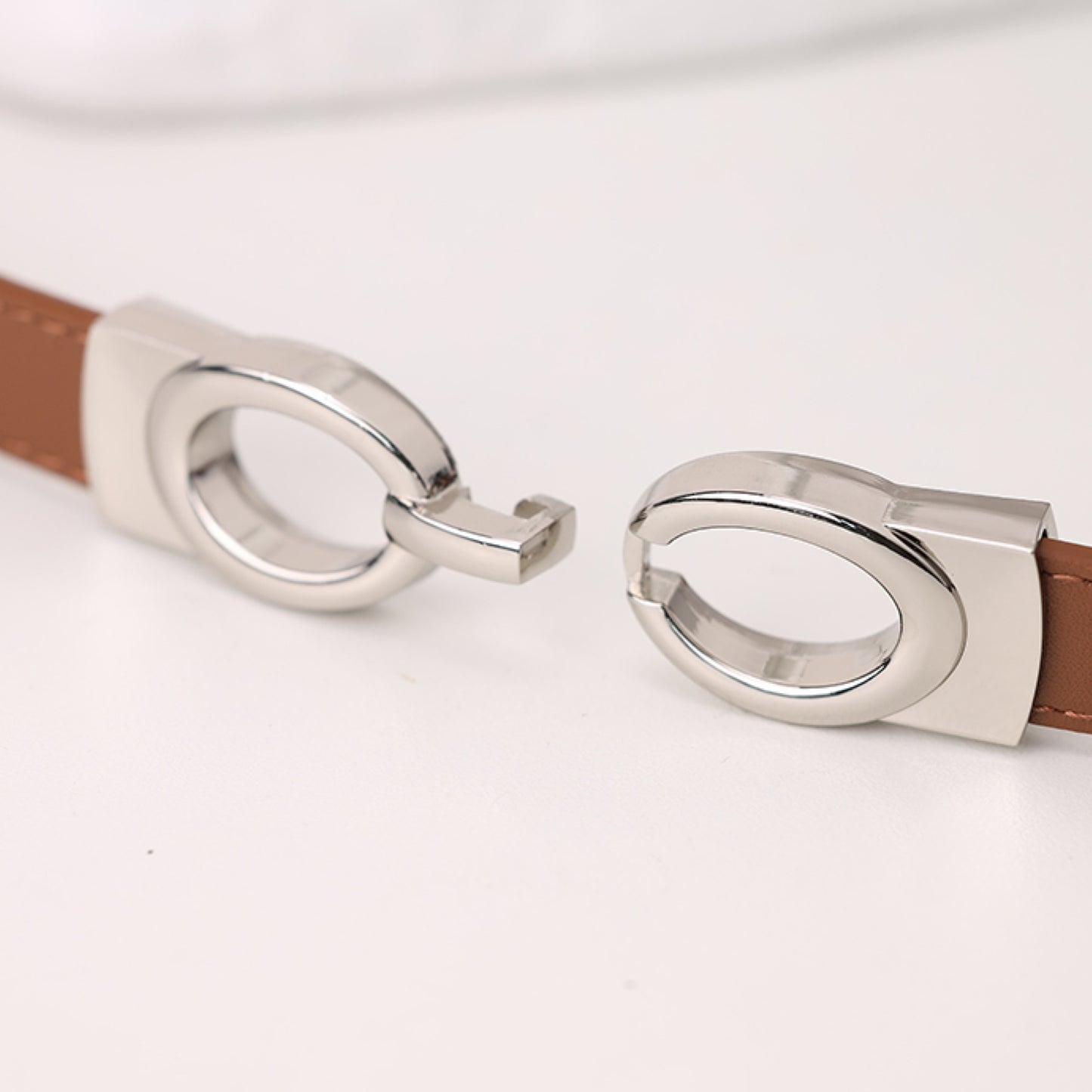 Brown leather belt with silver metal buckles on a light gray background