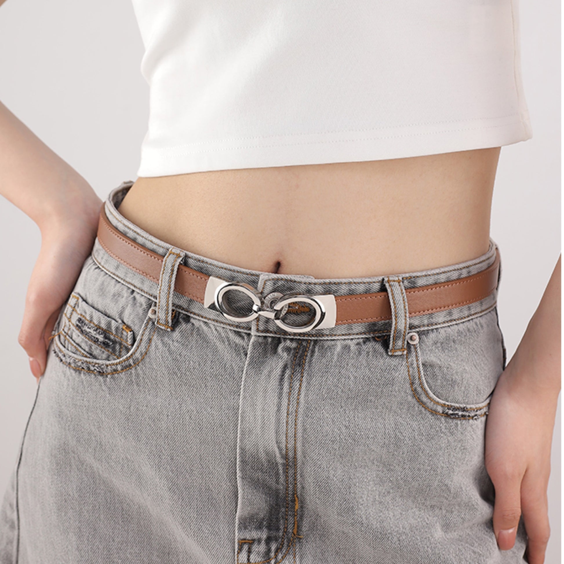 Person wearing gray jeans with a brown belt and white top on a light gray background