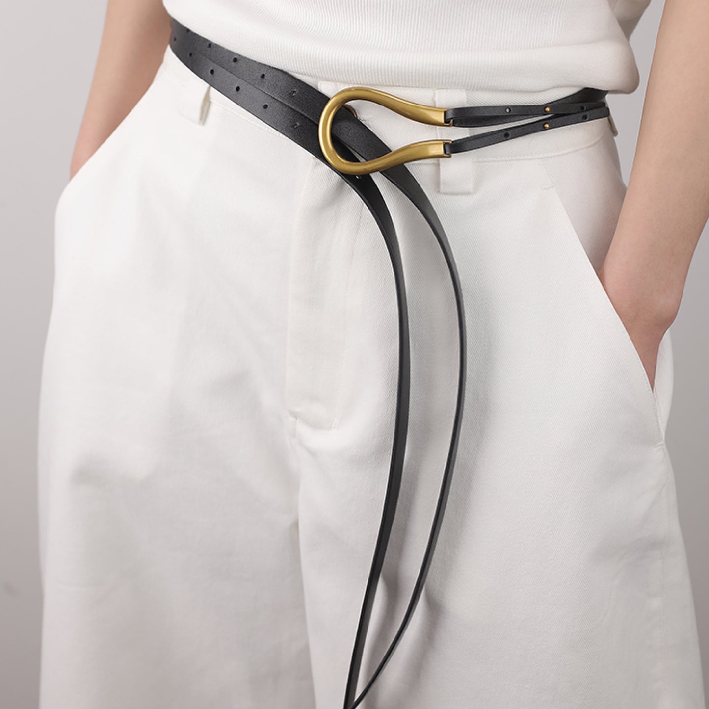 Black belt with a gold buckle worn by a person in white pants on a light gray background