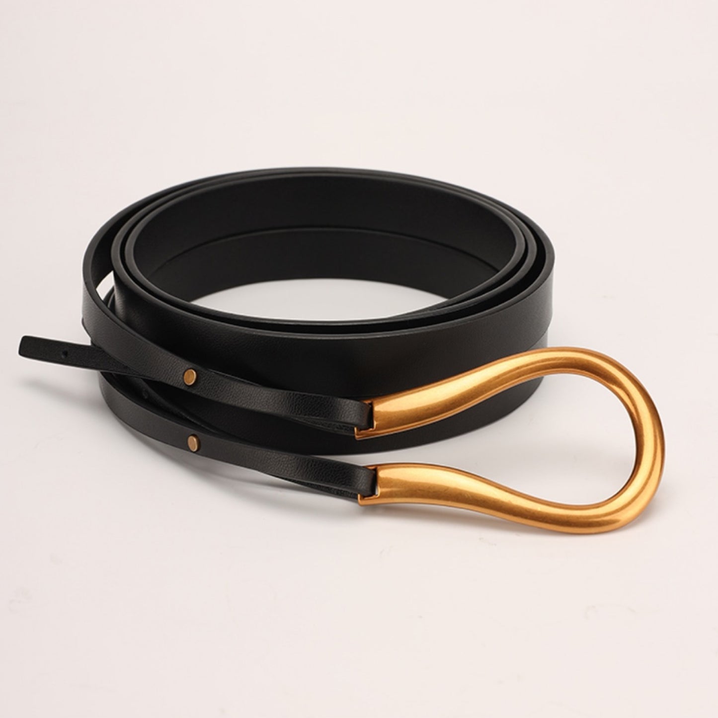 Black belt with gold hardware on a light beige background