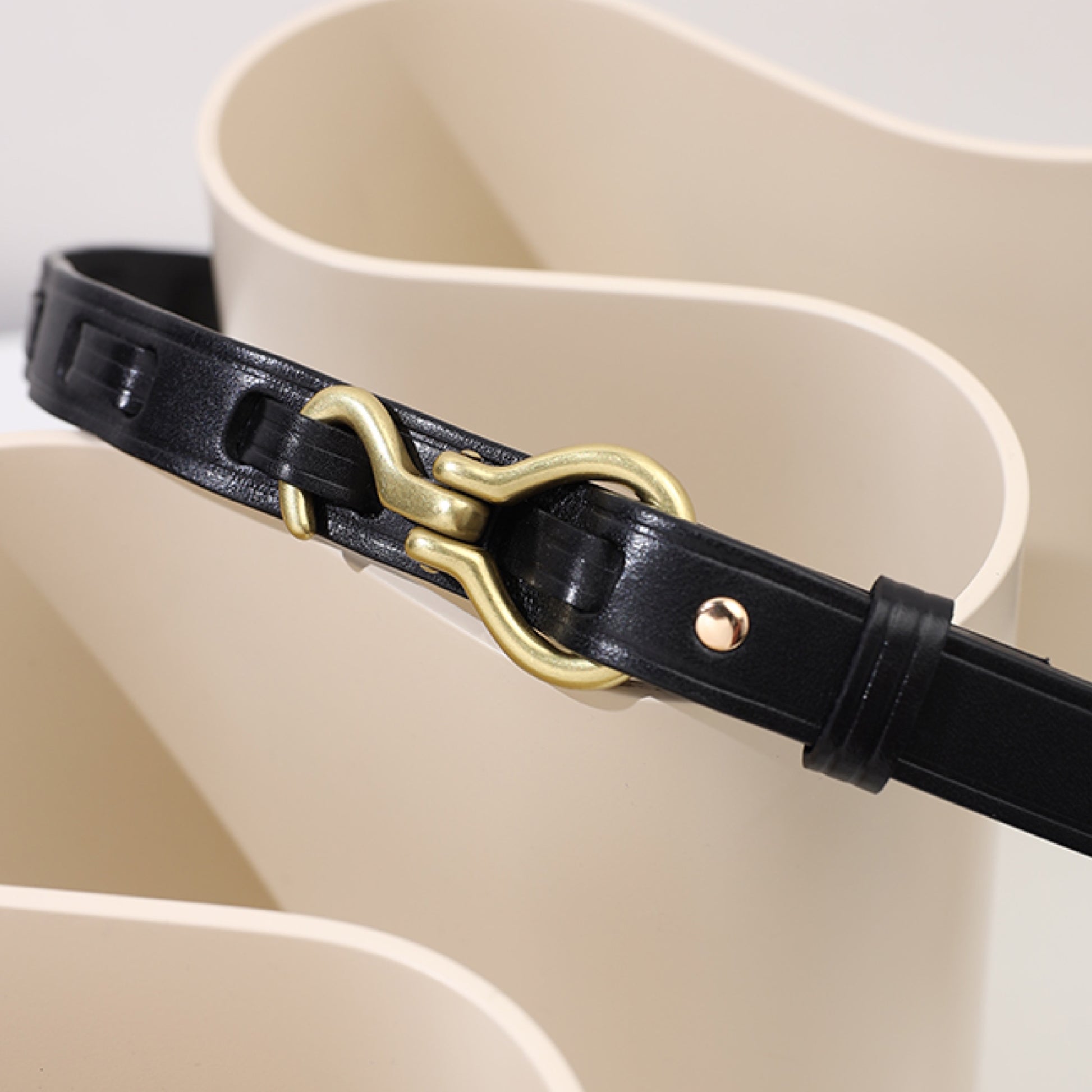 Black leather belt with a gold buckle on a beige background
