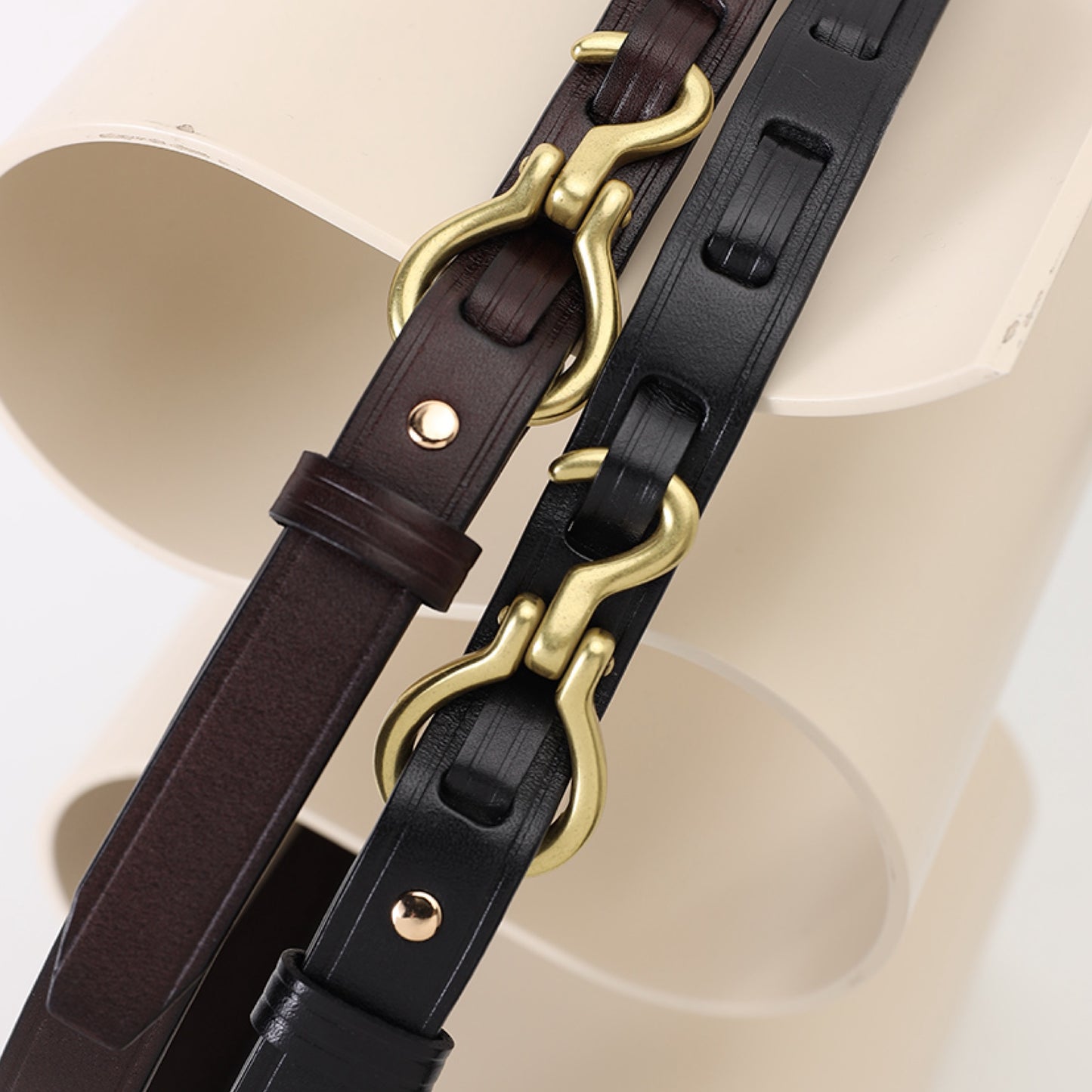 Two leather straps with gold hardware on a neutral background