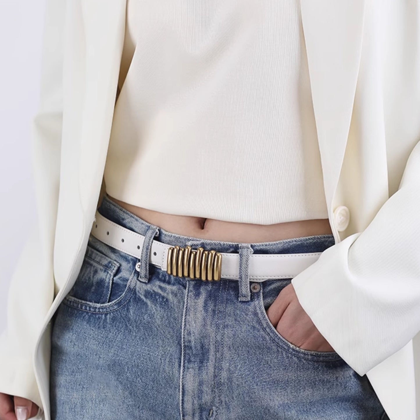 Person wearing a white blazer, white top, and blue jeans with a gold belt buckle.