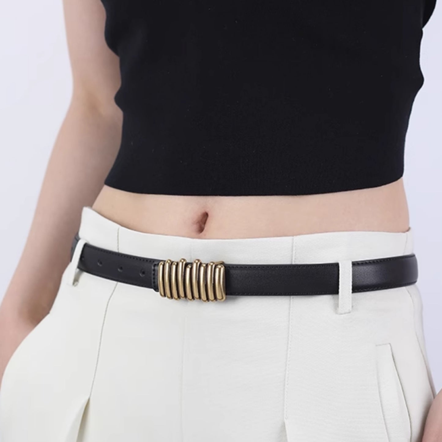 Person wearing a black belt with a gold buckle on white pants against a light purple background