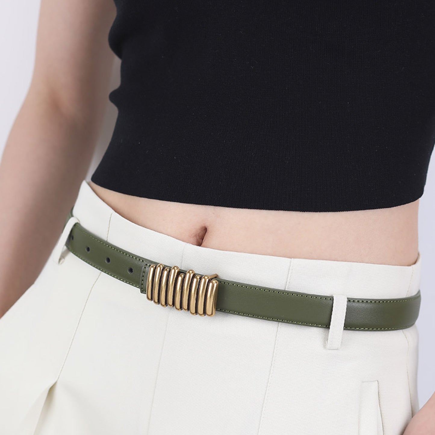 Person wearing a green belt with a gold buckle on white pants against a light background