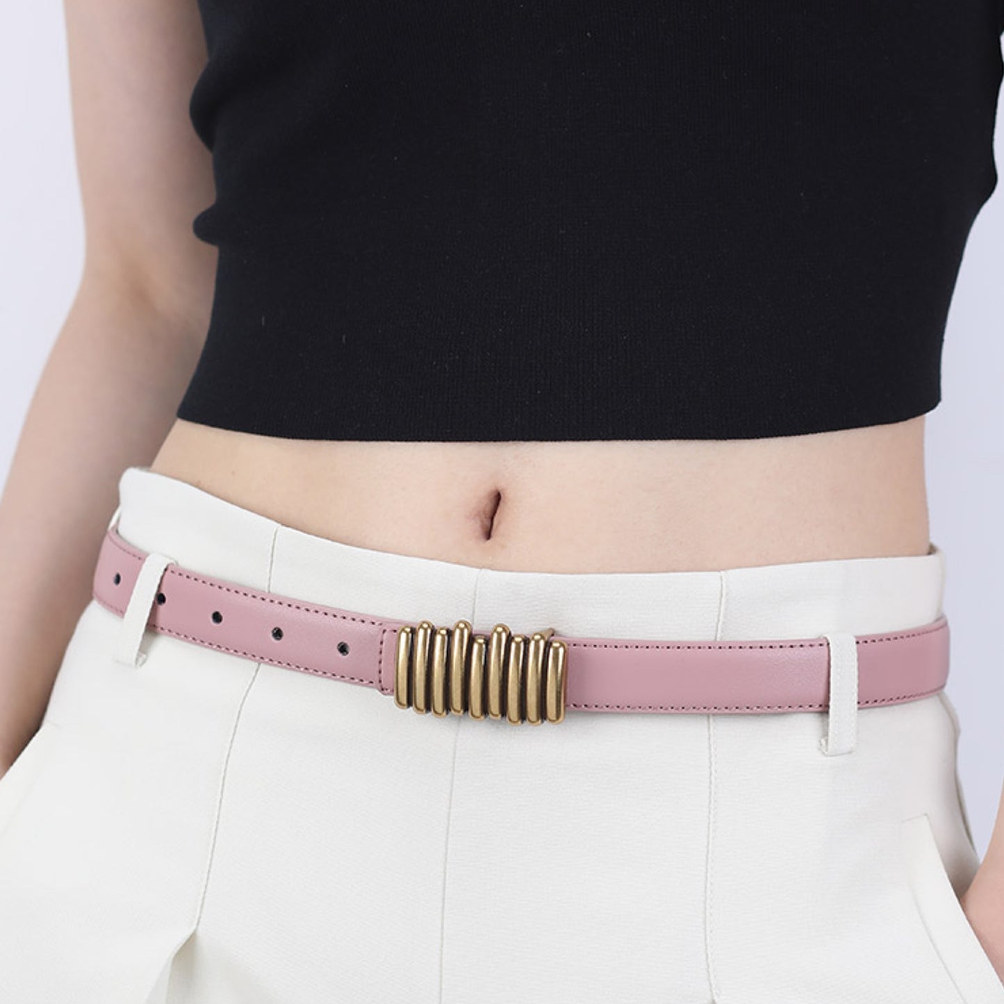 Person wearing a pink belt with a gold buckle on a plain background