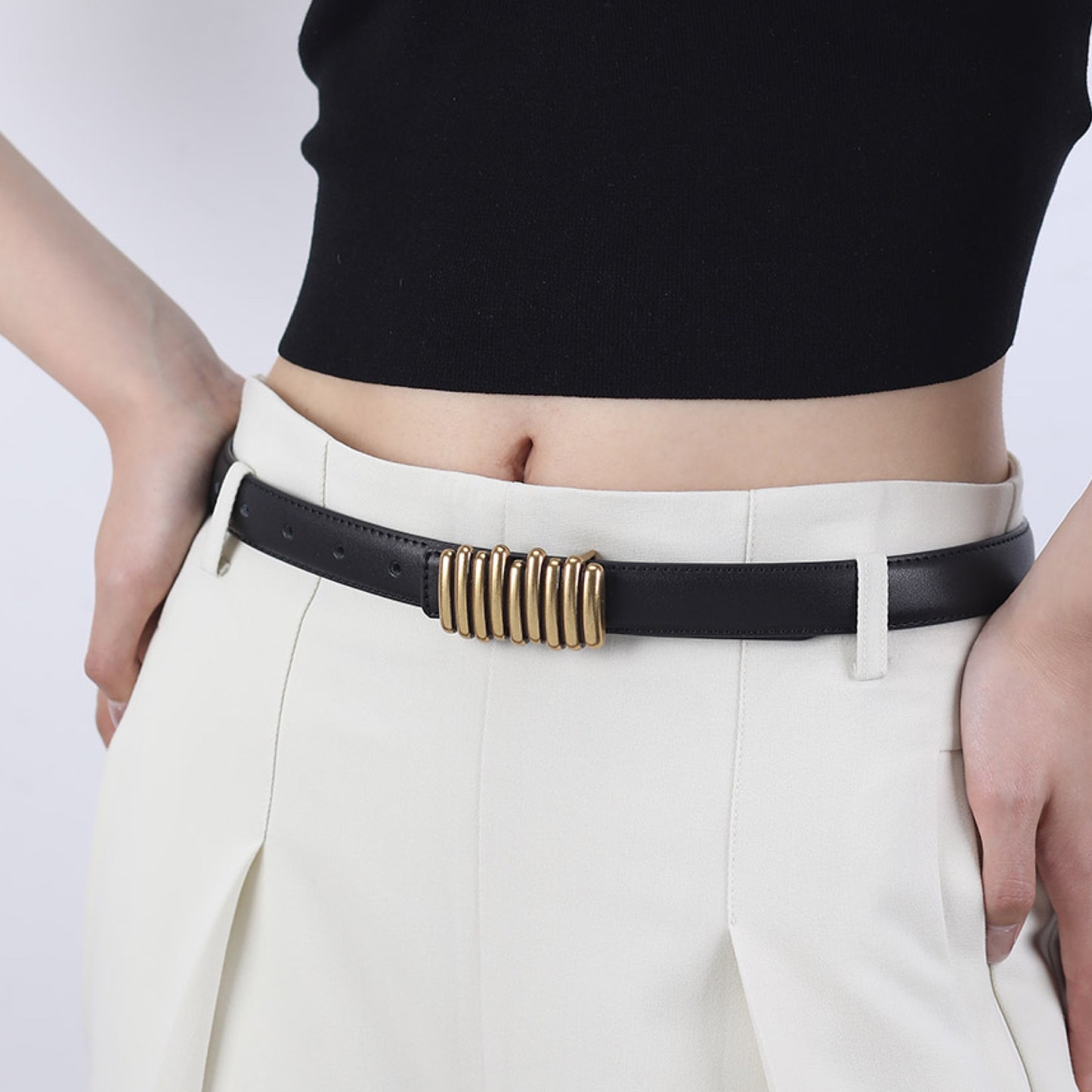 Person wearing a black belt with a gold buckle on white pants against a gray background