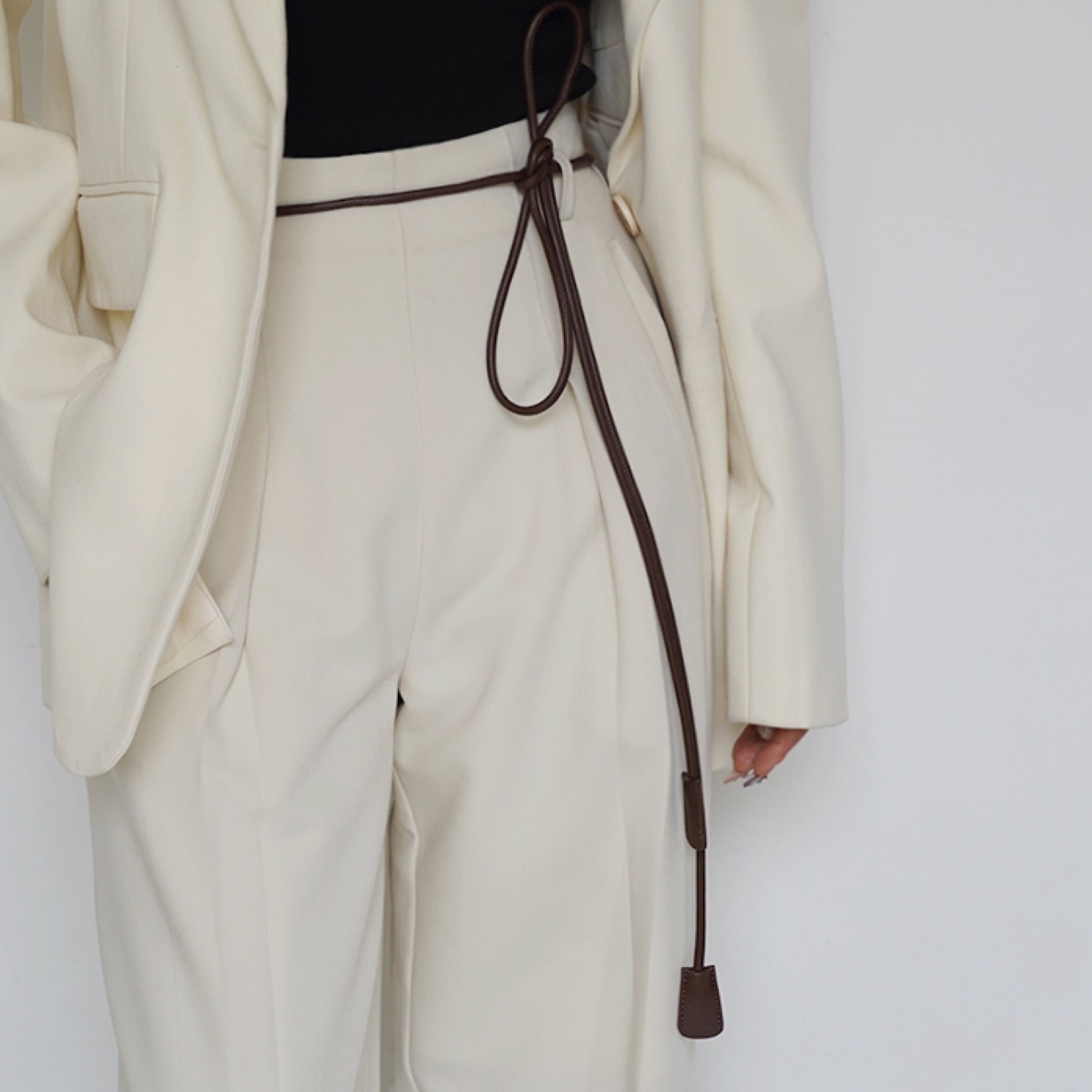Person wearing a cream coat and pants with a brown belt on a white background