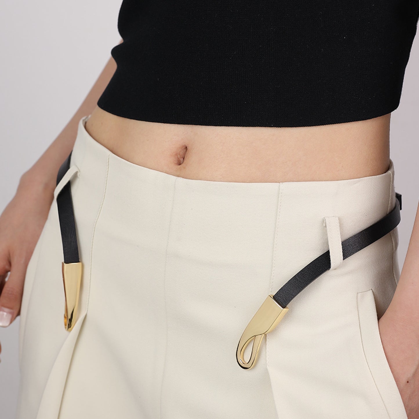 Person wearing beige pants with a black belt featuring gold hardware on a plain background