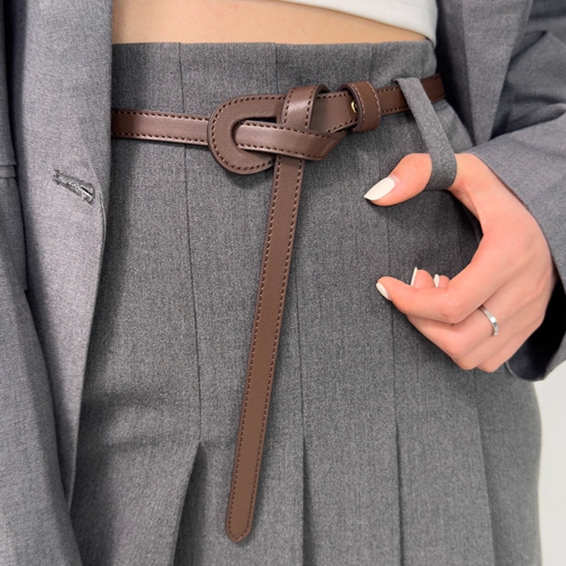 Person wearing a gray coat with a brown belt and beige background