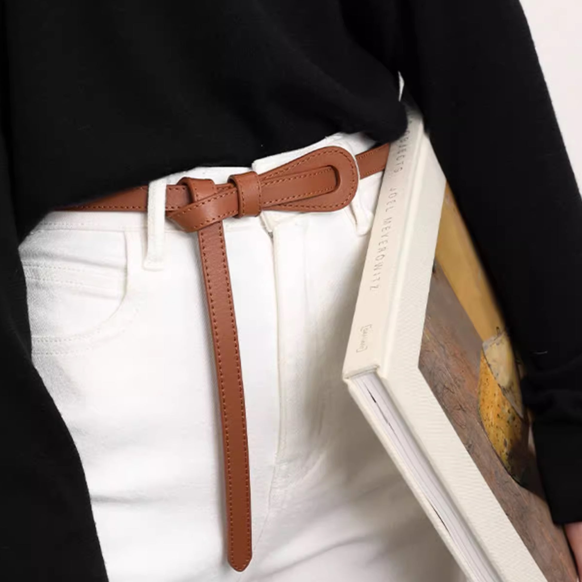 Close-up of a person wearing a brown belt with a book on a white surface.