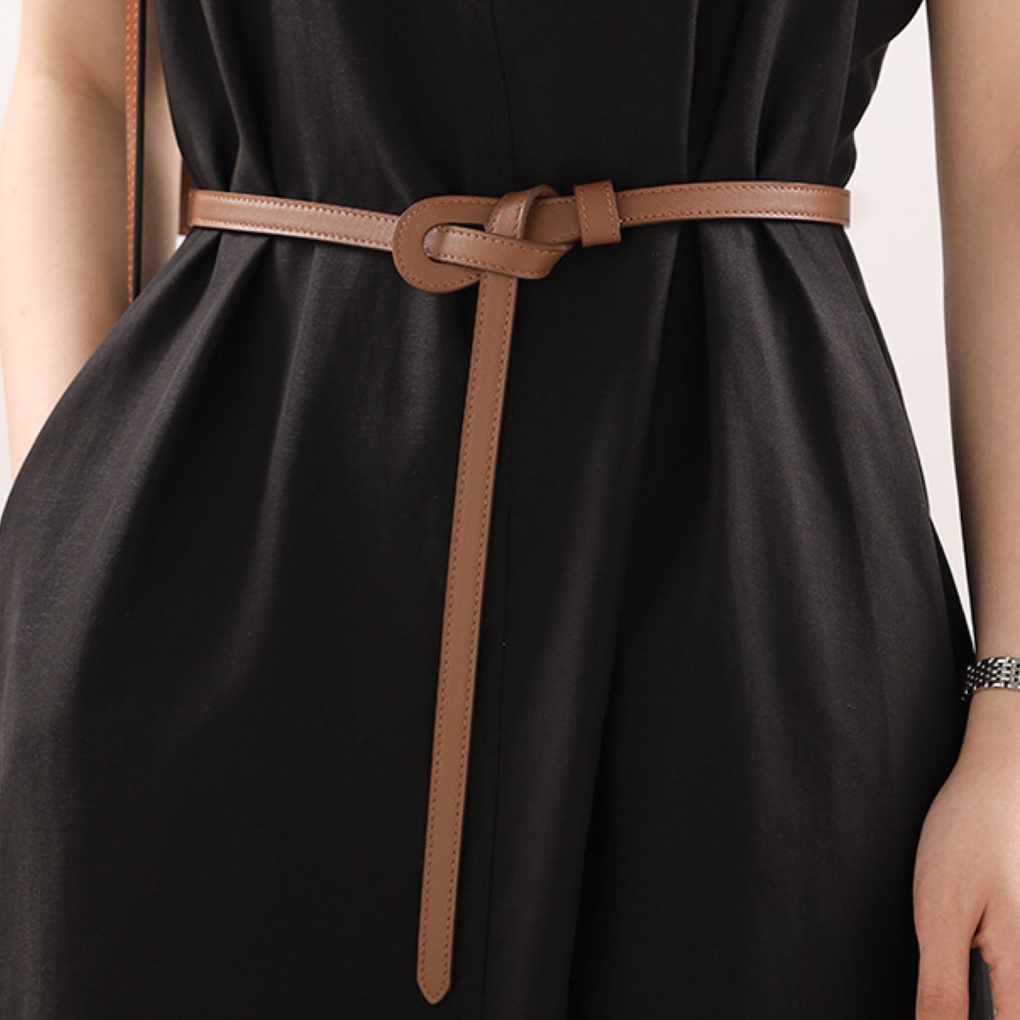 Black dress with a brown belt on a neutral background