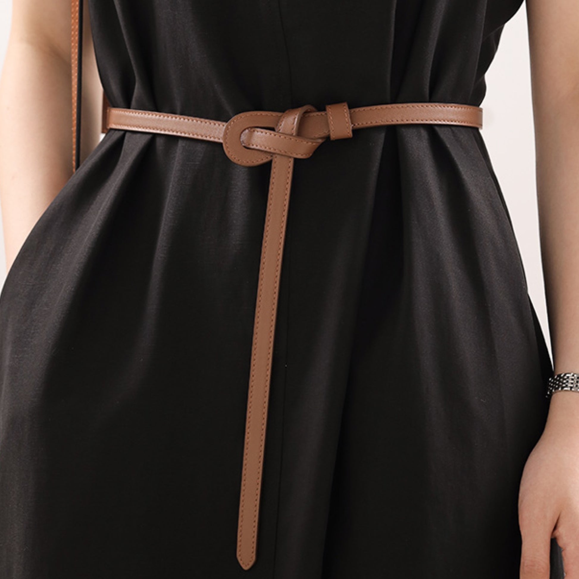 Black dress with a brown belt on a neutral background
