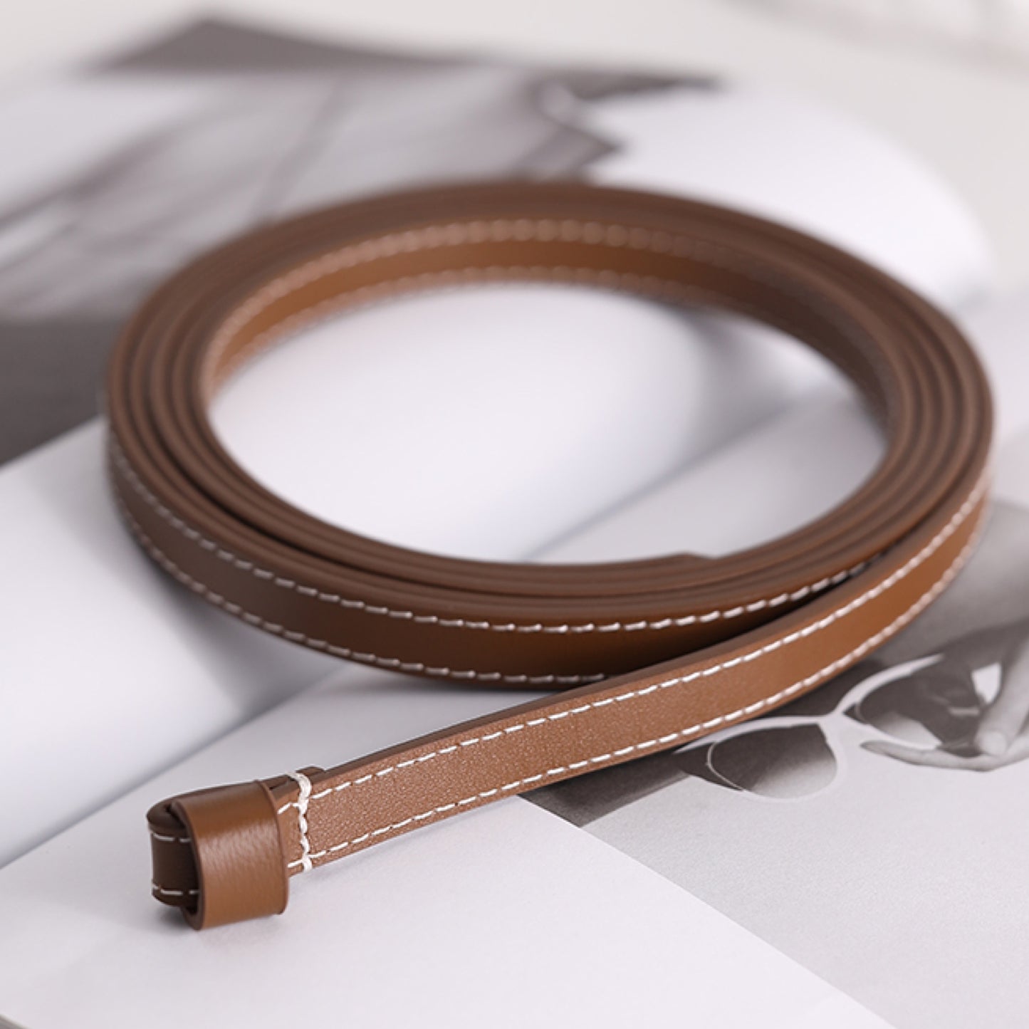 Brown leather belt with white stitching on a light background