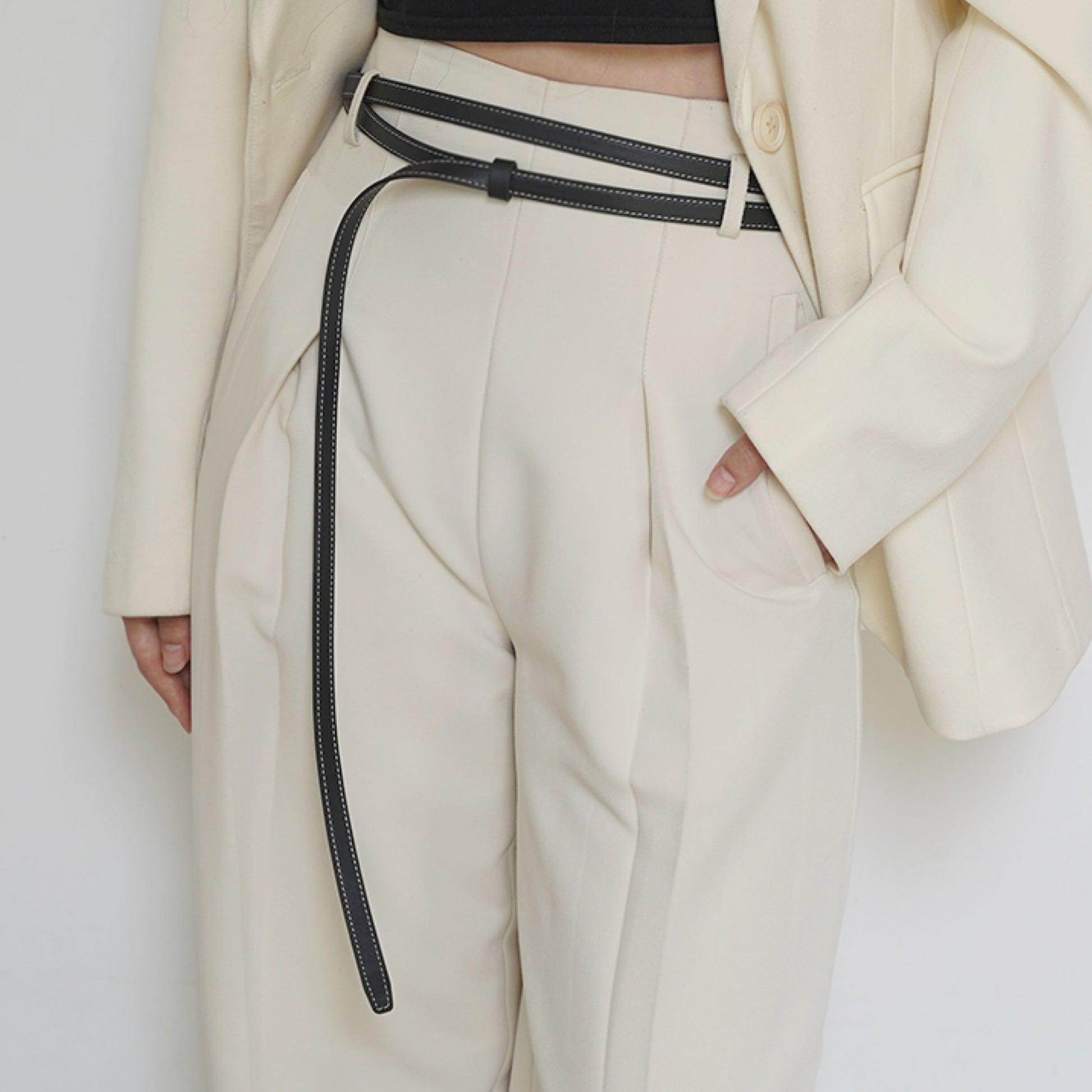 Person wearing a white coat and beige pants with a black belt against a white background