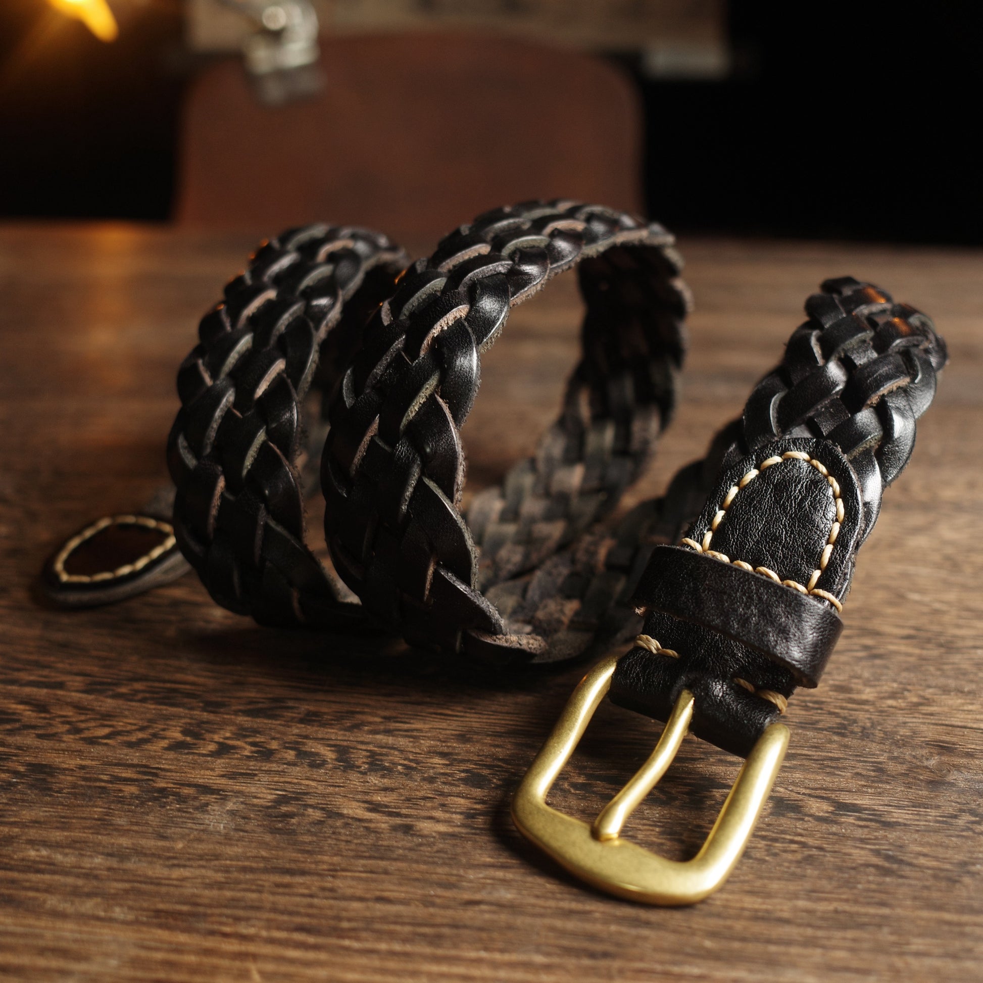 Black braided leather belt with a gold buckle on a wooden surface