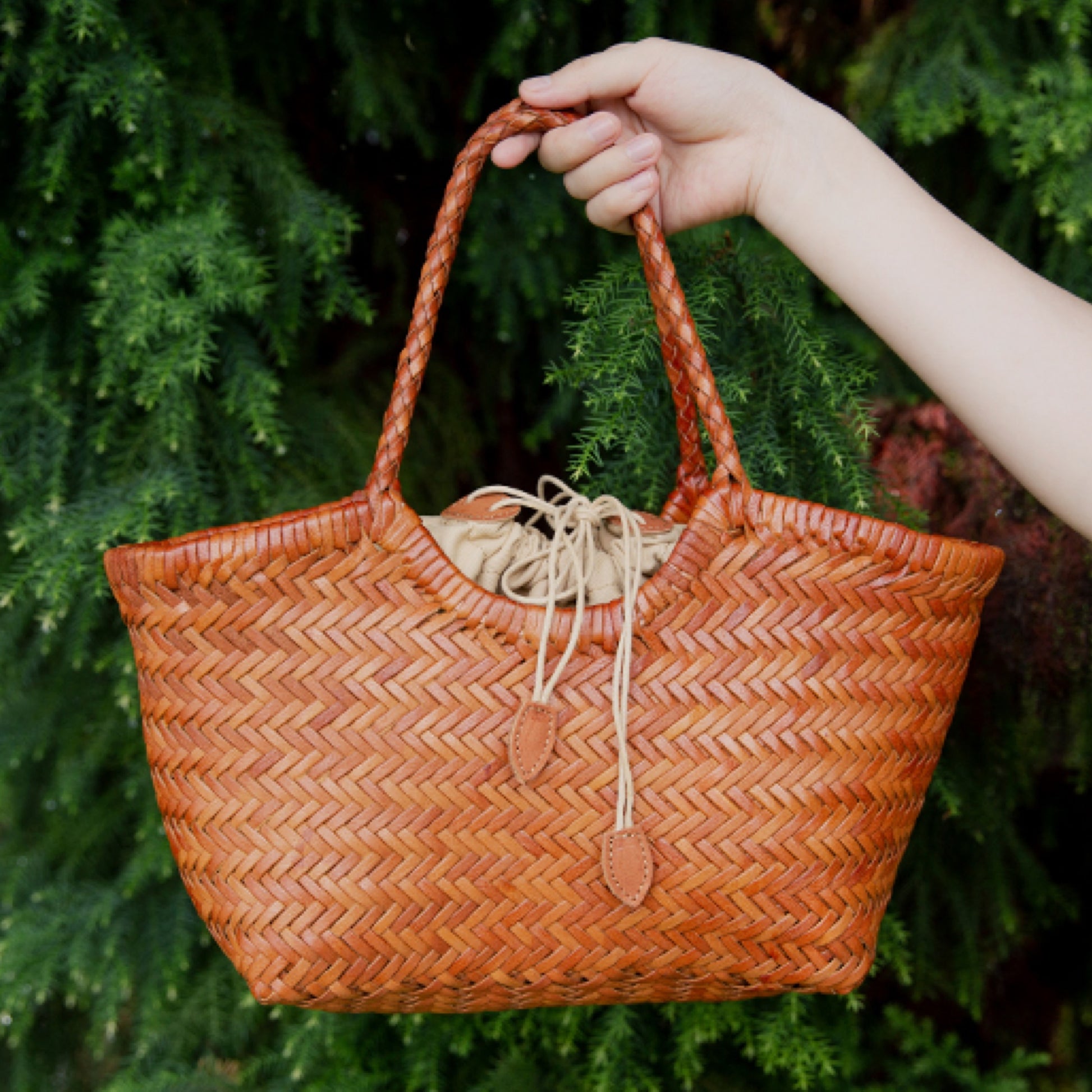 Hand holding a woven brown bag against a green leafy background