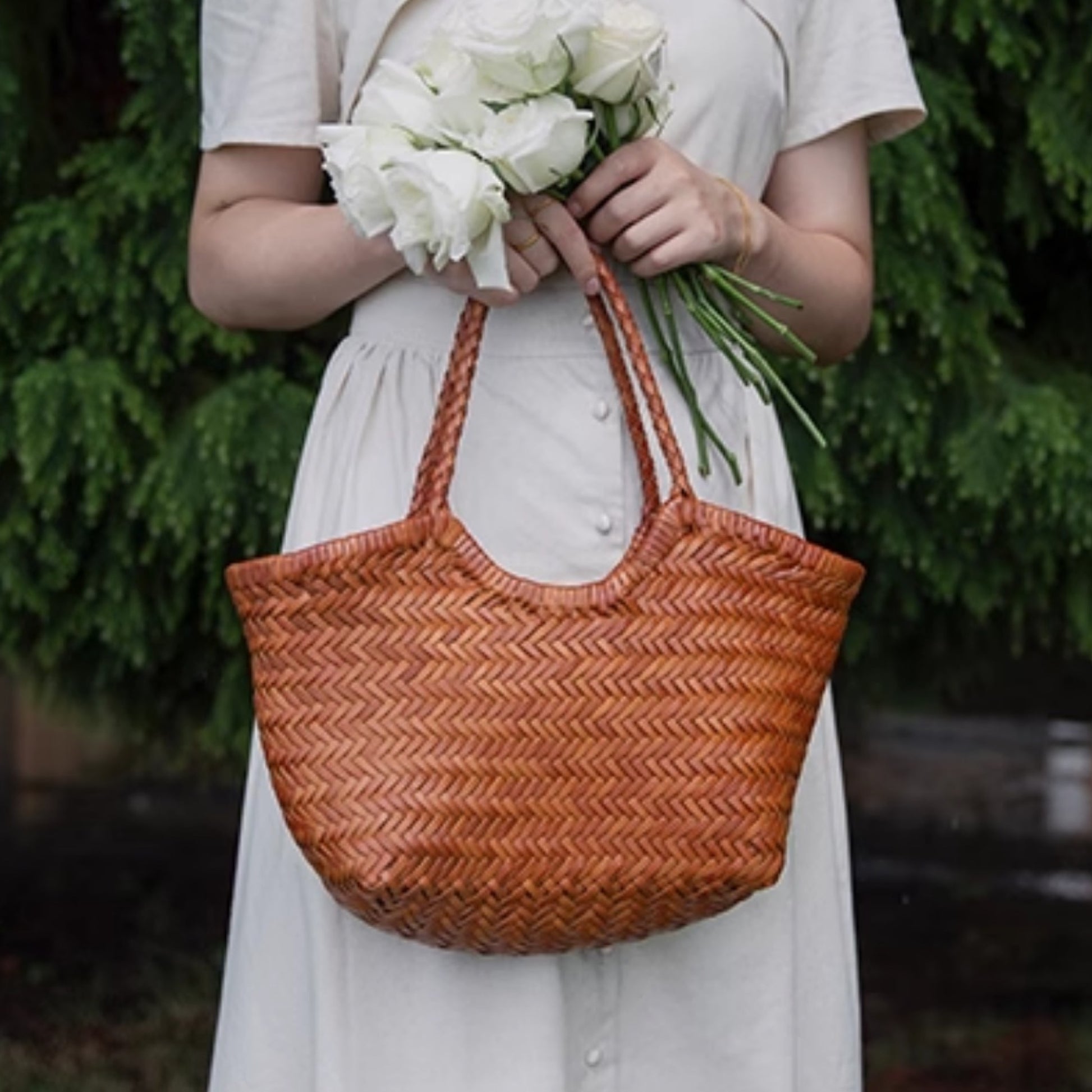 Person holding a woven brown bag and white flowers against a blurred green background