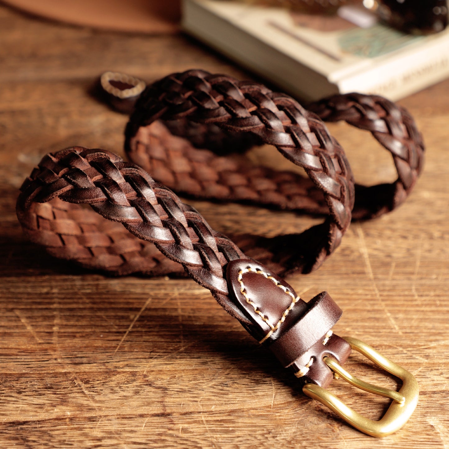 Brown braided leather belt with brass buckle on a wooden surface