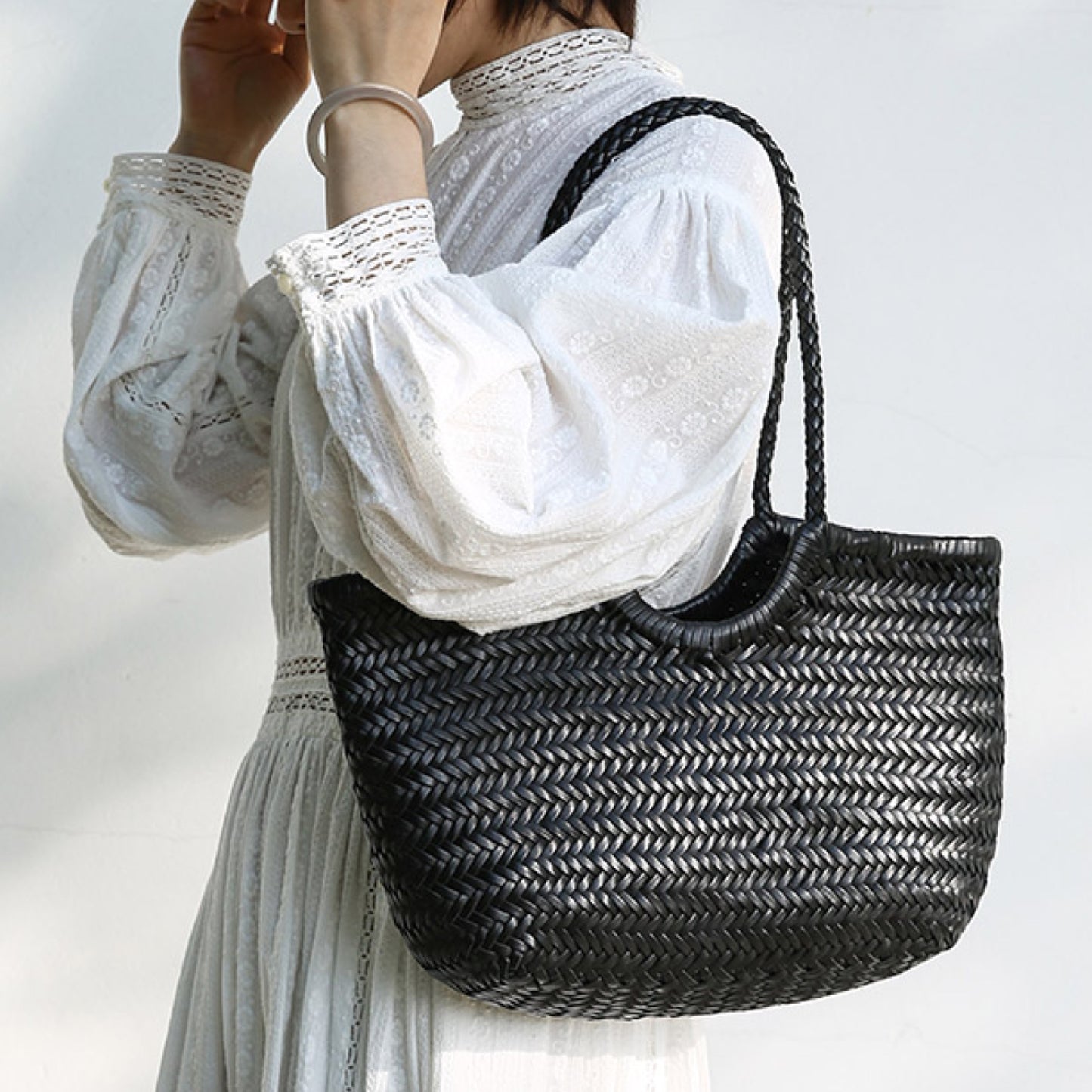 Person holding a black woven handbag against a white background