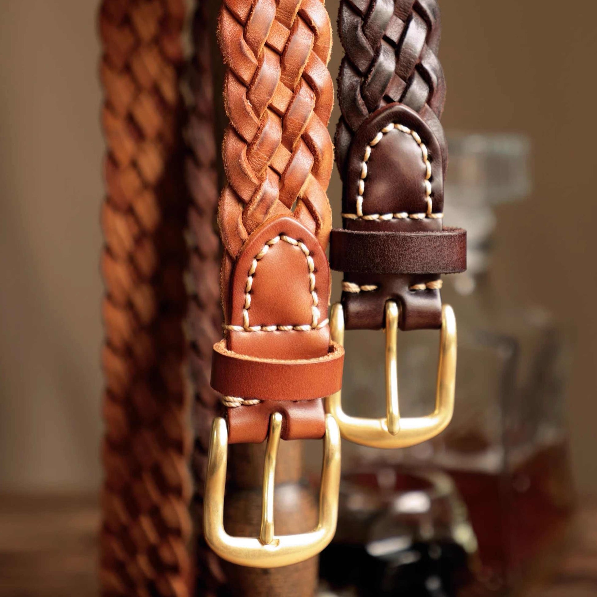 Two braided leather belts with brass buckles on a blurred background