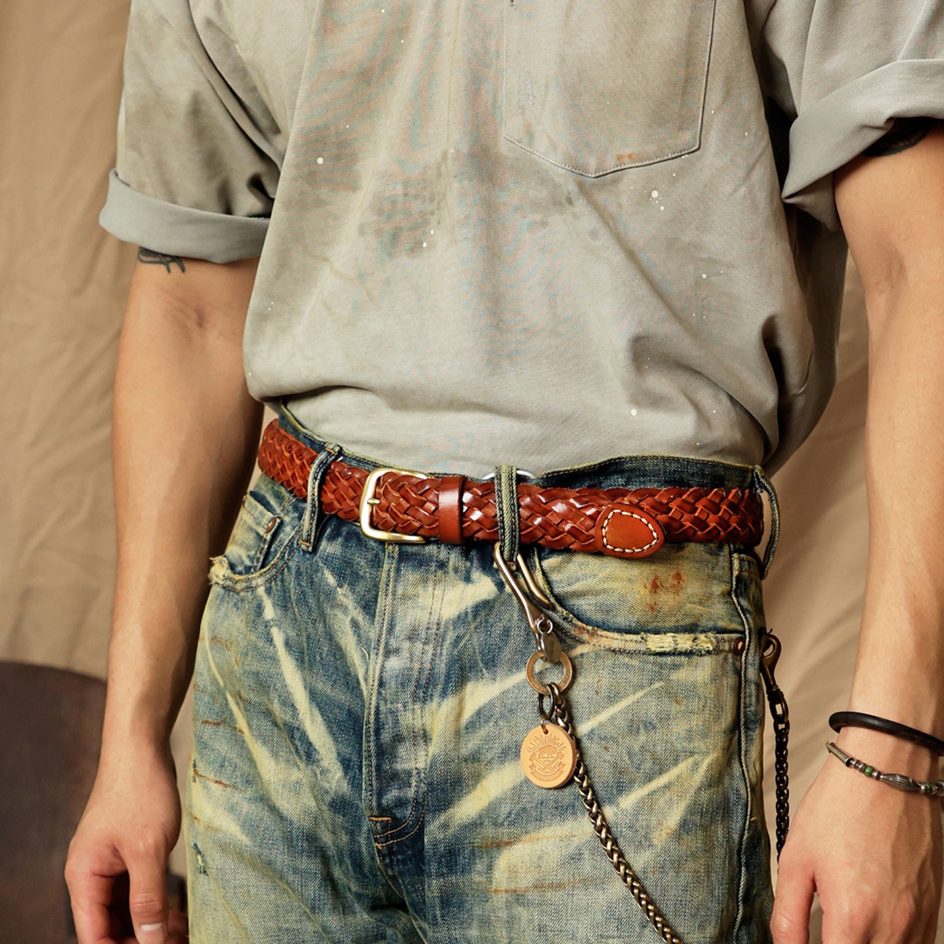 Person wearing a brown leather belt with a silver buckle and a keychain, standing against a neutral background.