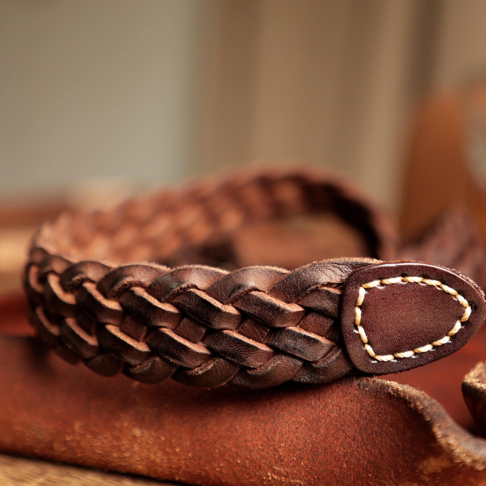 Brown braided leather belt with a buckle on a wooden surface