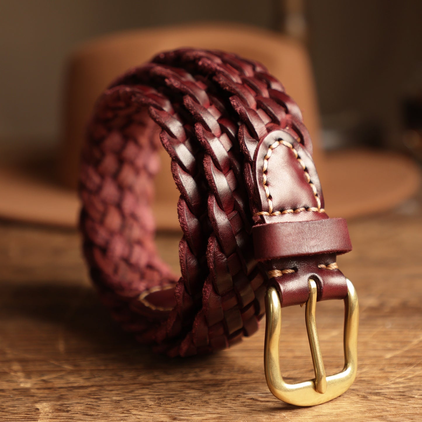 Woven leather belt with a gold buckle on a wooden surface