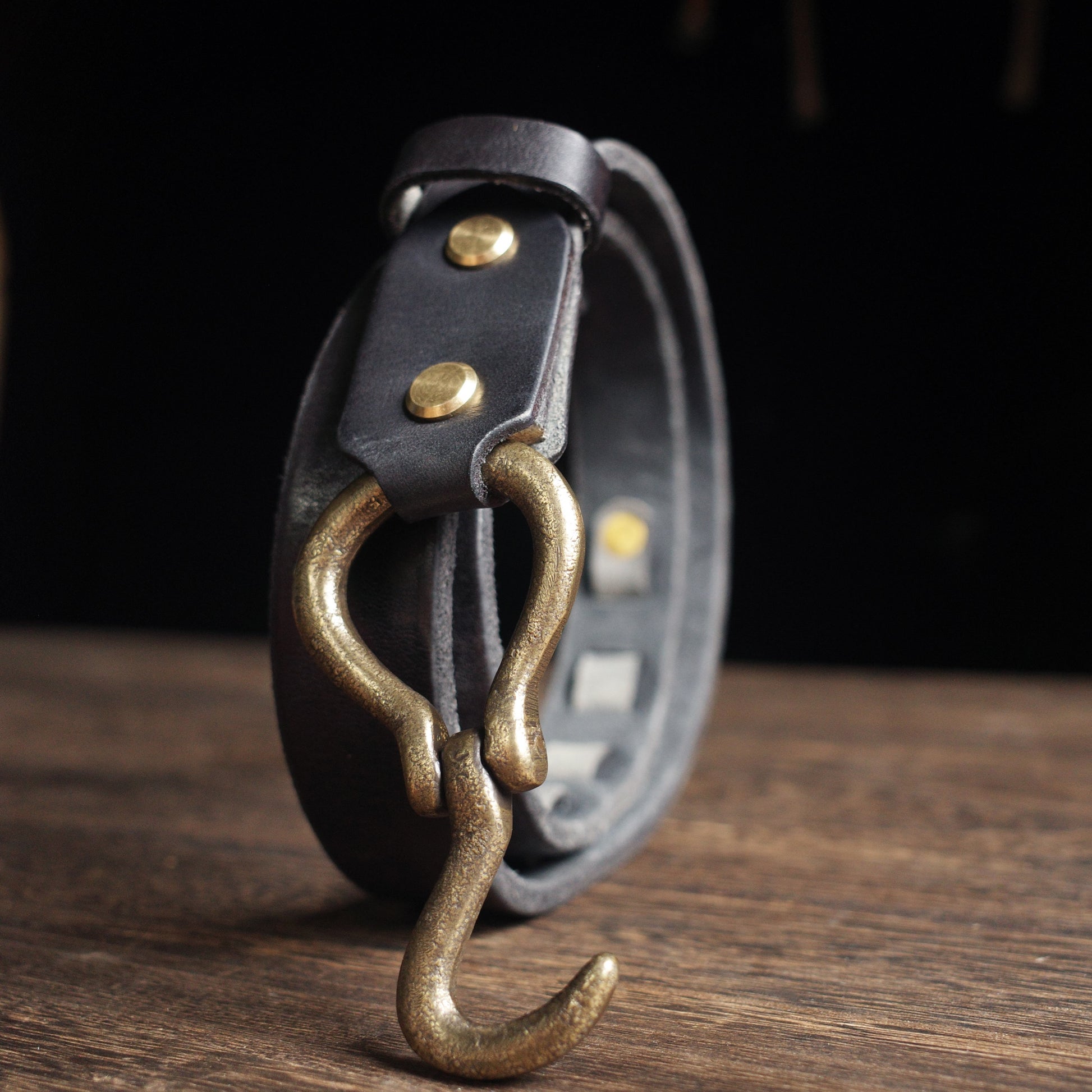 Black leather belt with brass hook on a wooden surface
