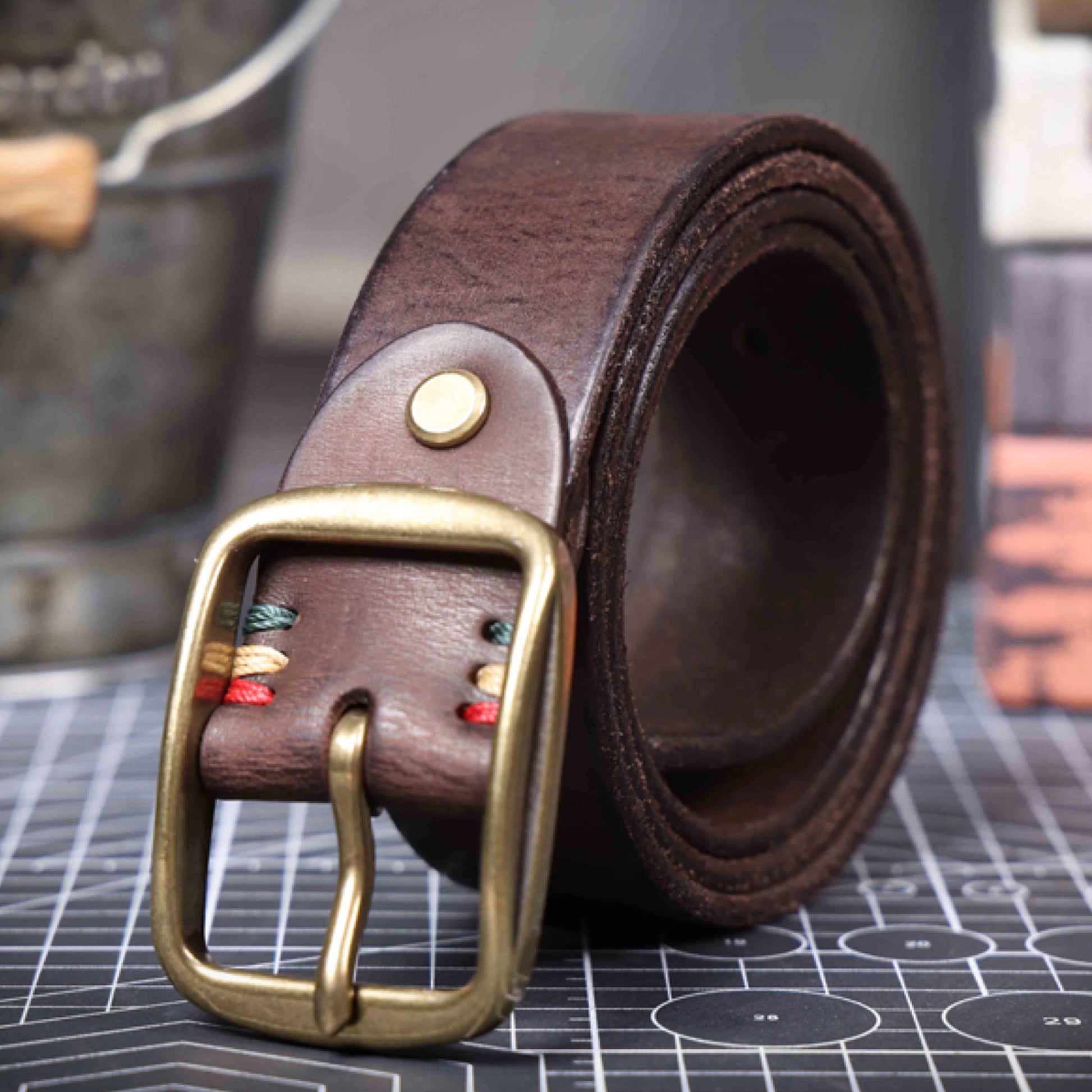 Brown leather belt with brass buckle on a grid surface
