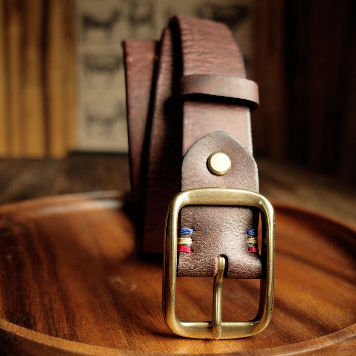 Brown leather belt with a gold buckle on a wooden surface