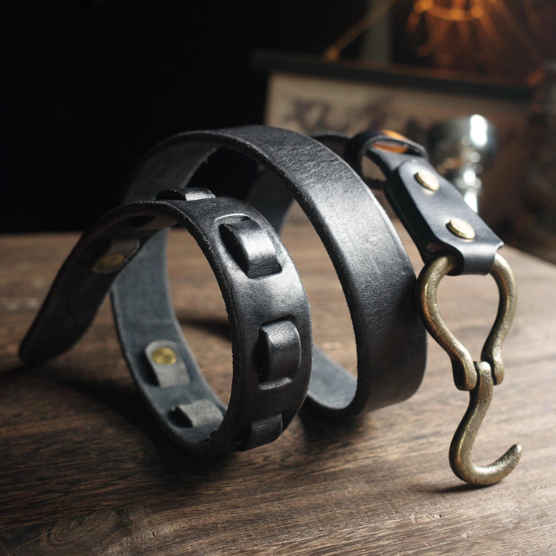 Two black leather bracelets with metal hooks on a wooden surface