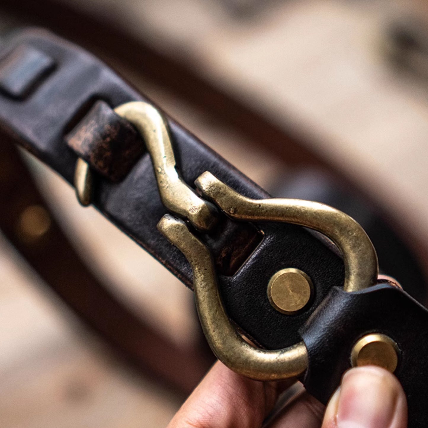 Close-up of a leather belt with brass buckle held by a hand.
