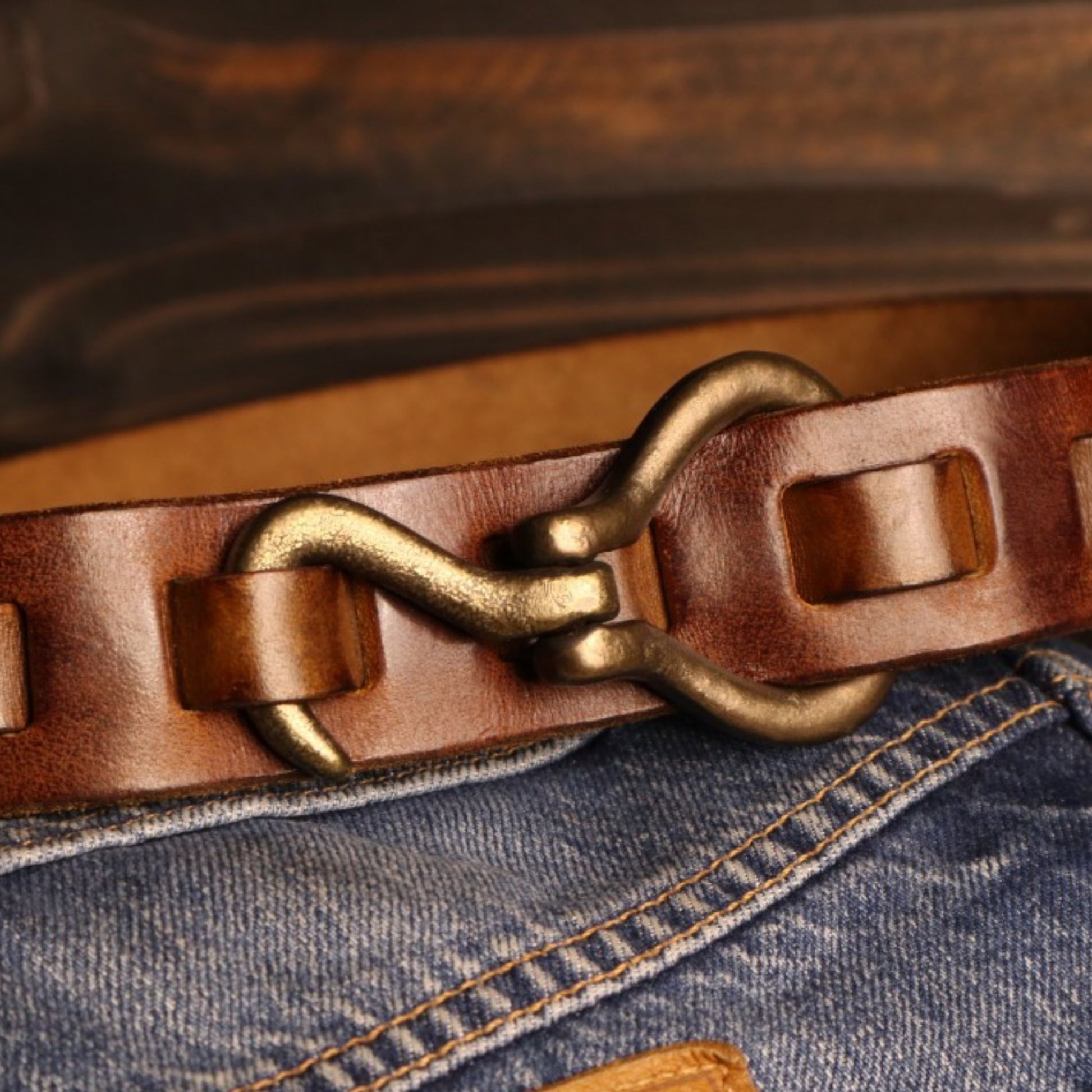 Close-up of a brown leather belt with a brass buckle on blue jeans.