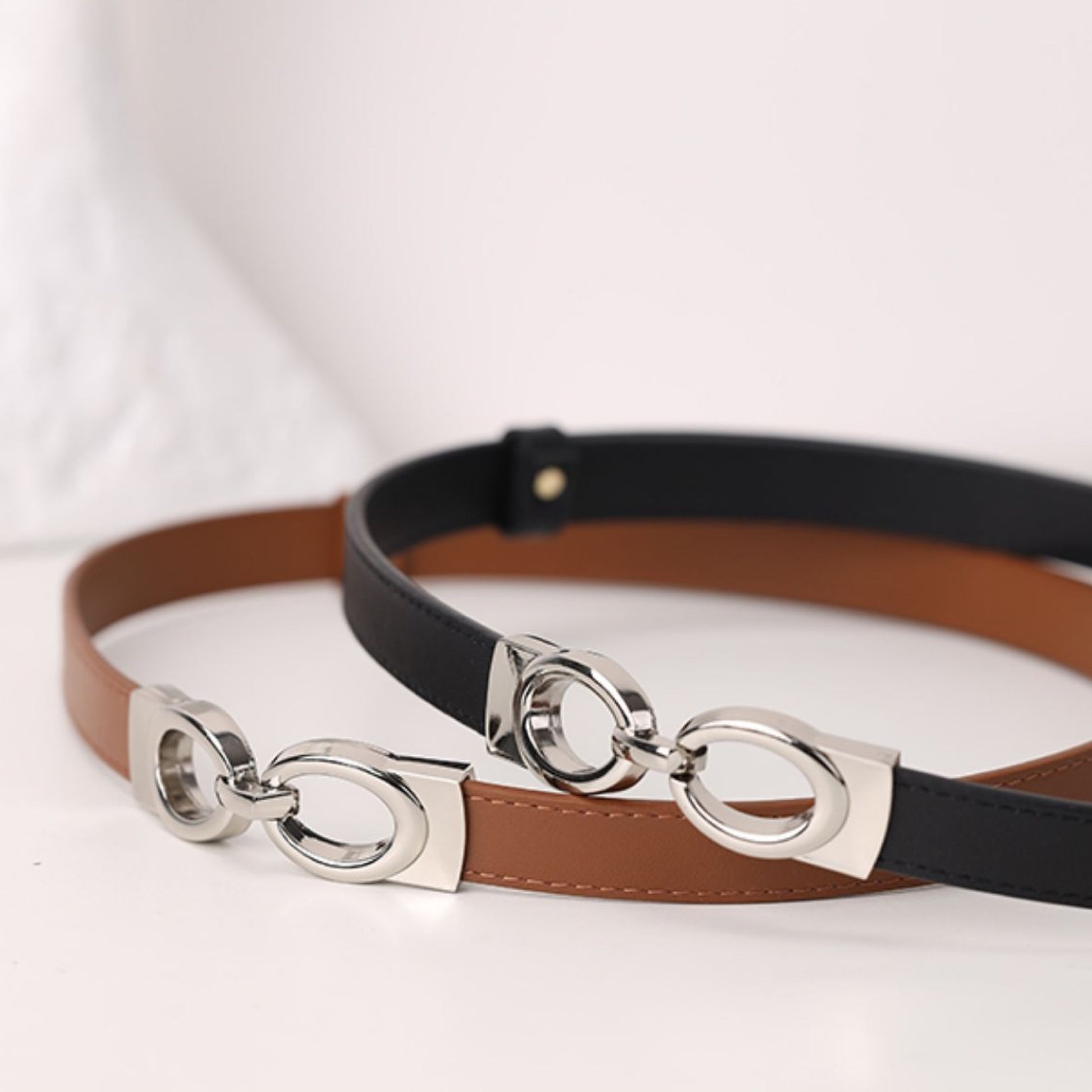 Two belts with silver ring designs on a white background
