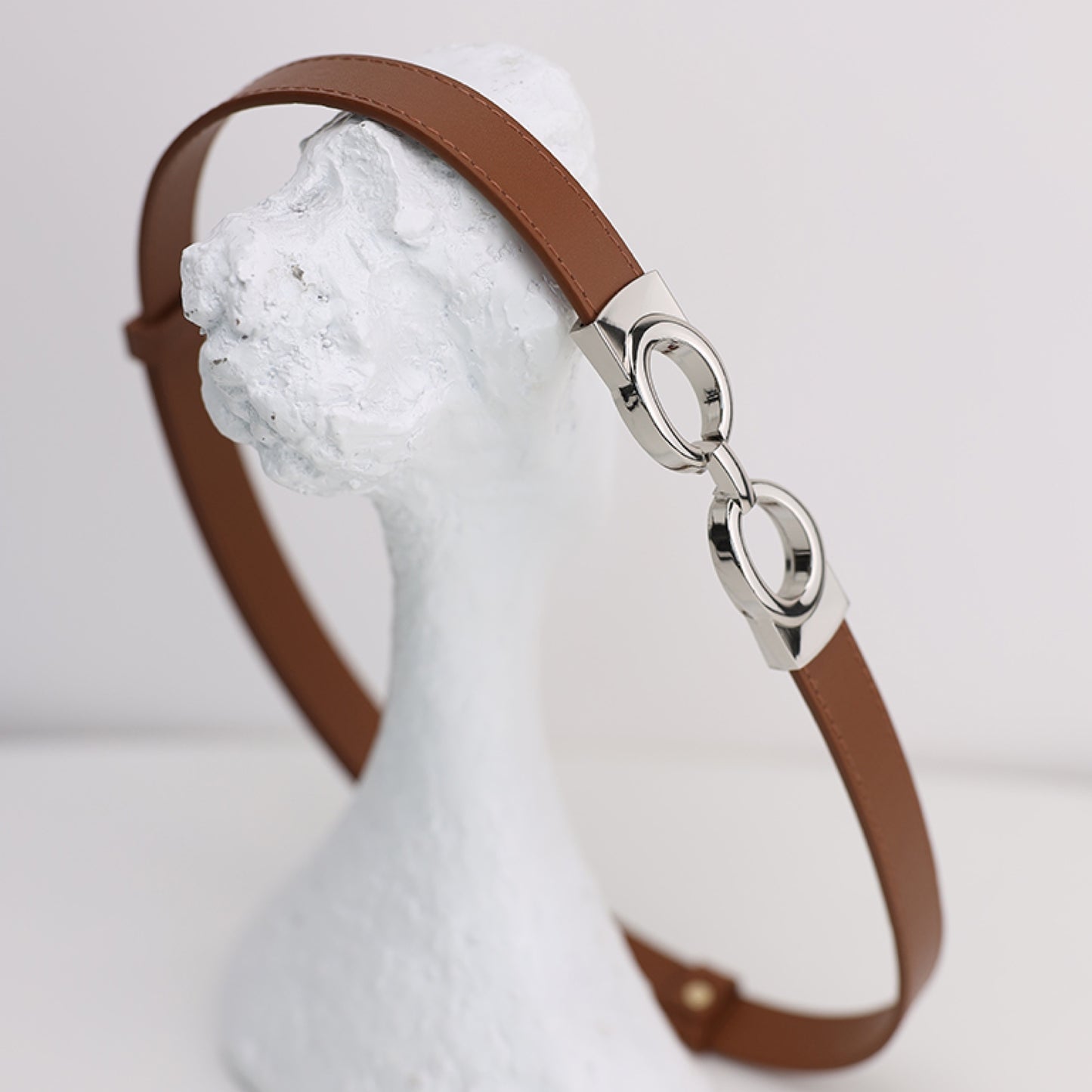 Brown leather headband with silver clasp on a mannequin head against a white background