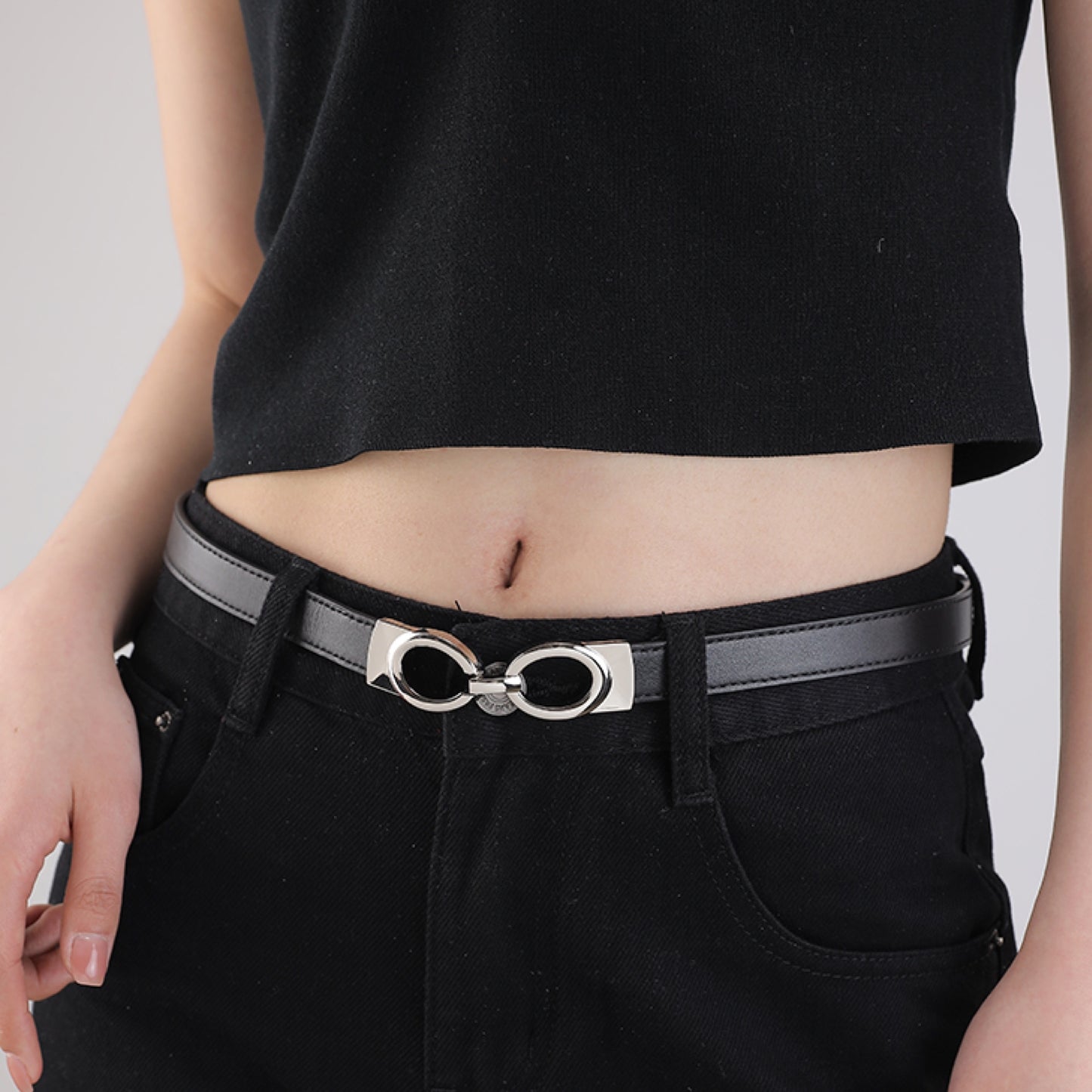 Person wearing a black belt with a silver buckle on a plain background