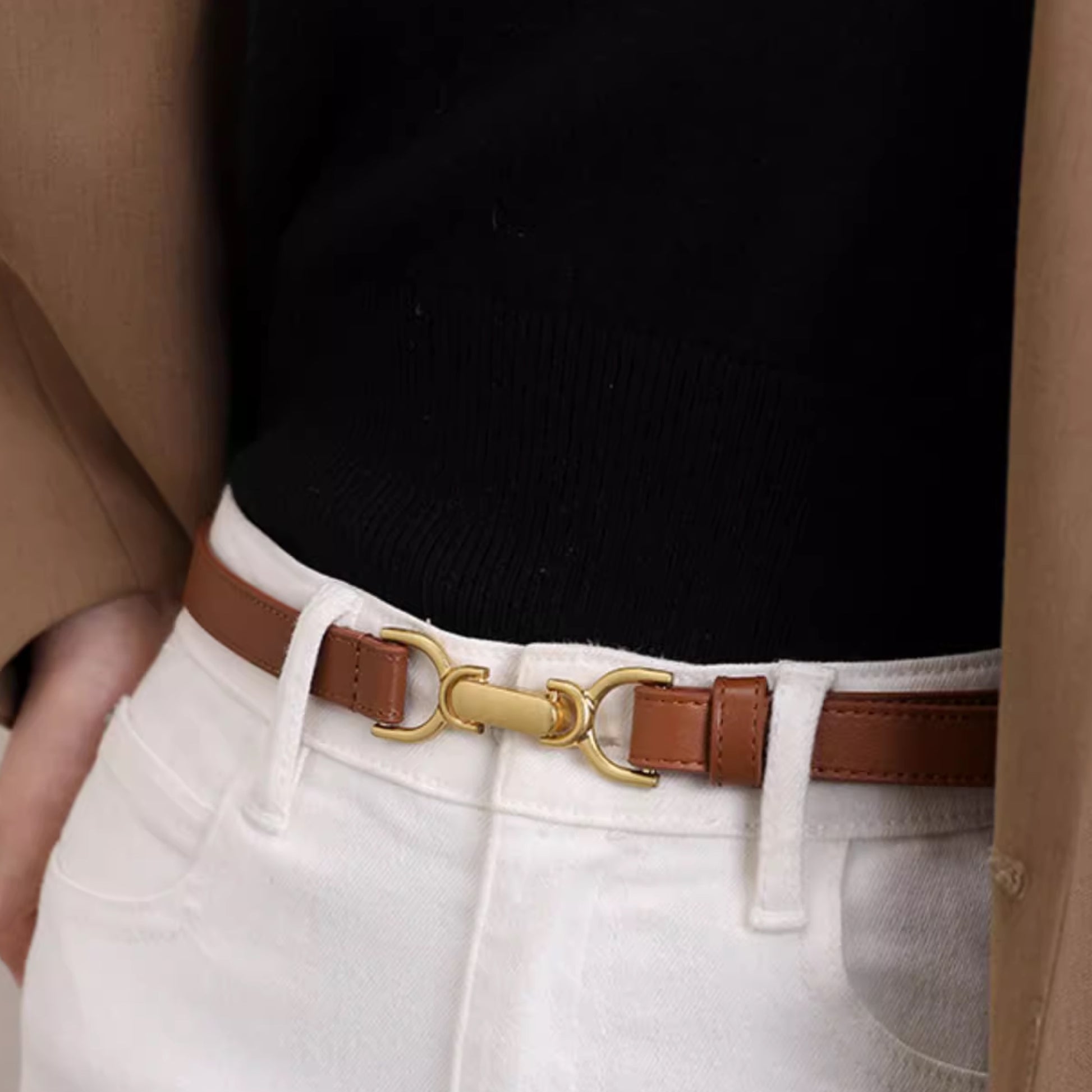Close-up of a person wearing a brown belt with a gold buckle, white pants, and a black top.